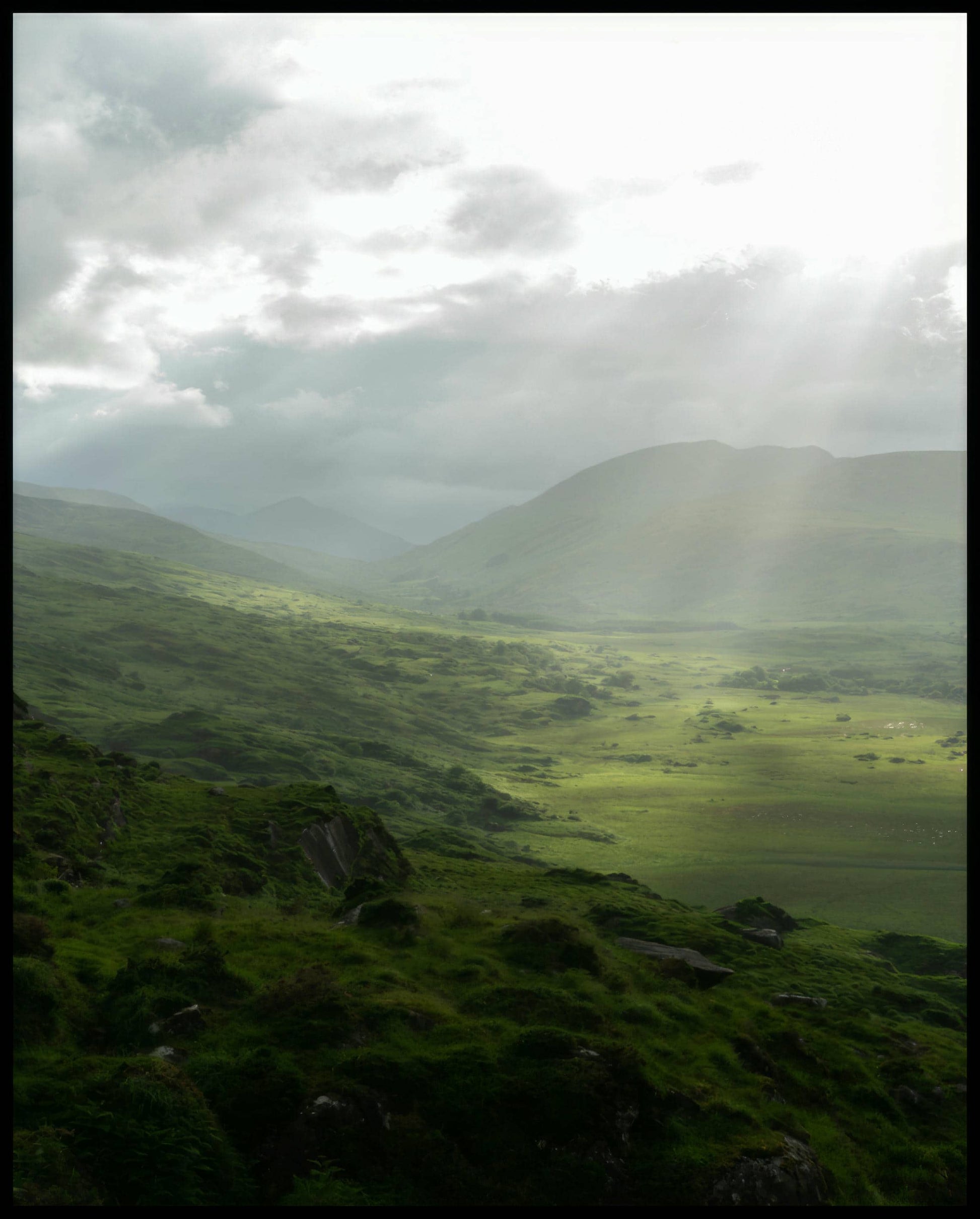 Ein Leinwandbild von einer grünen Landschaft in Irland mit Sonnenstrahlen.