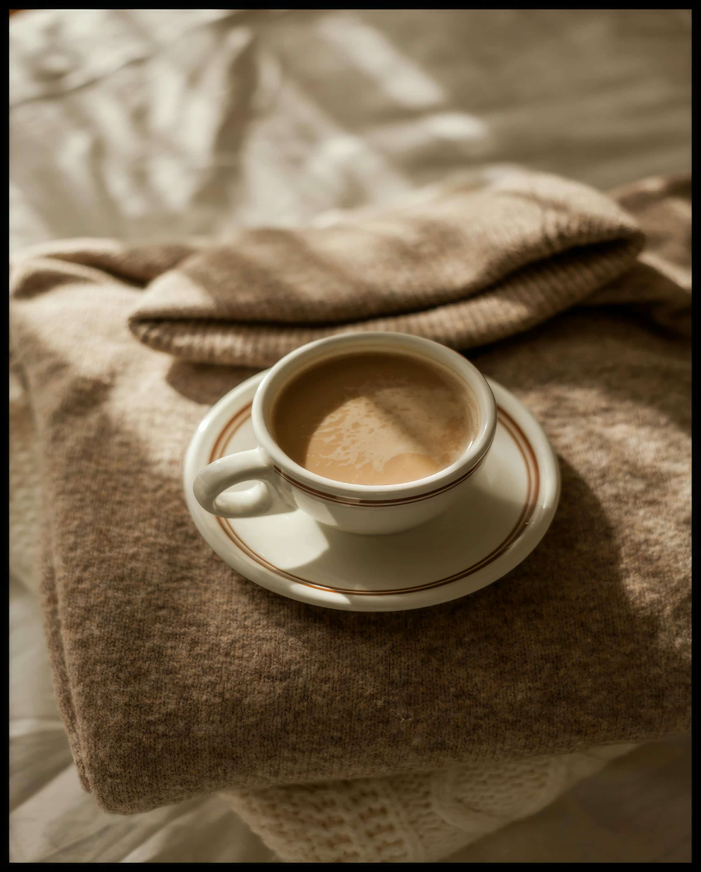 Ein Leinwandbild von einer Tasse Kaffee auf einem gemütlichen, beigen Pullover.
