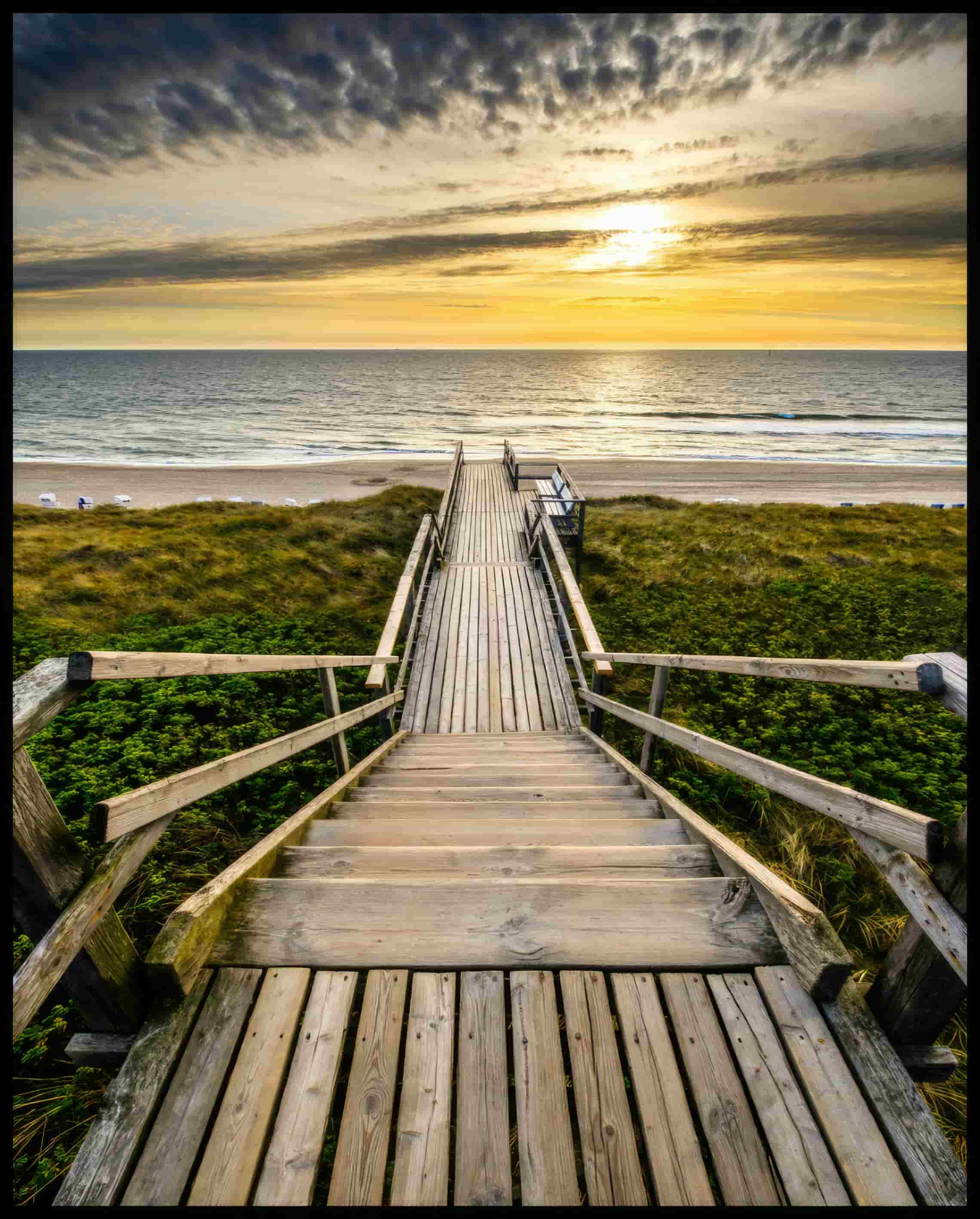 Leinwandbild von einem Holzsteg mit einer Treppe, der durch Dünen zum Strand führt.