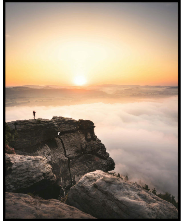 Ein Poster von einem Bergsteiger, der bei Sonnenaufgang auf einer Klippe steht.
