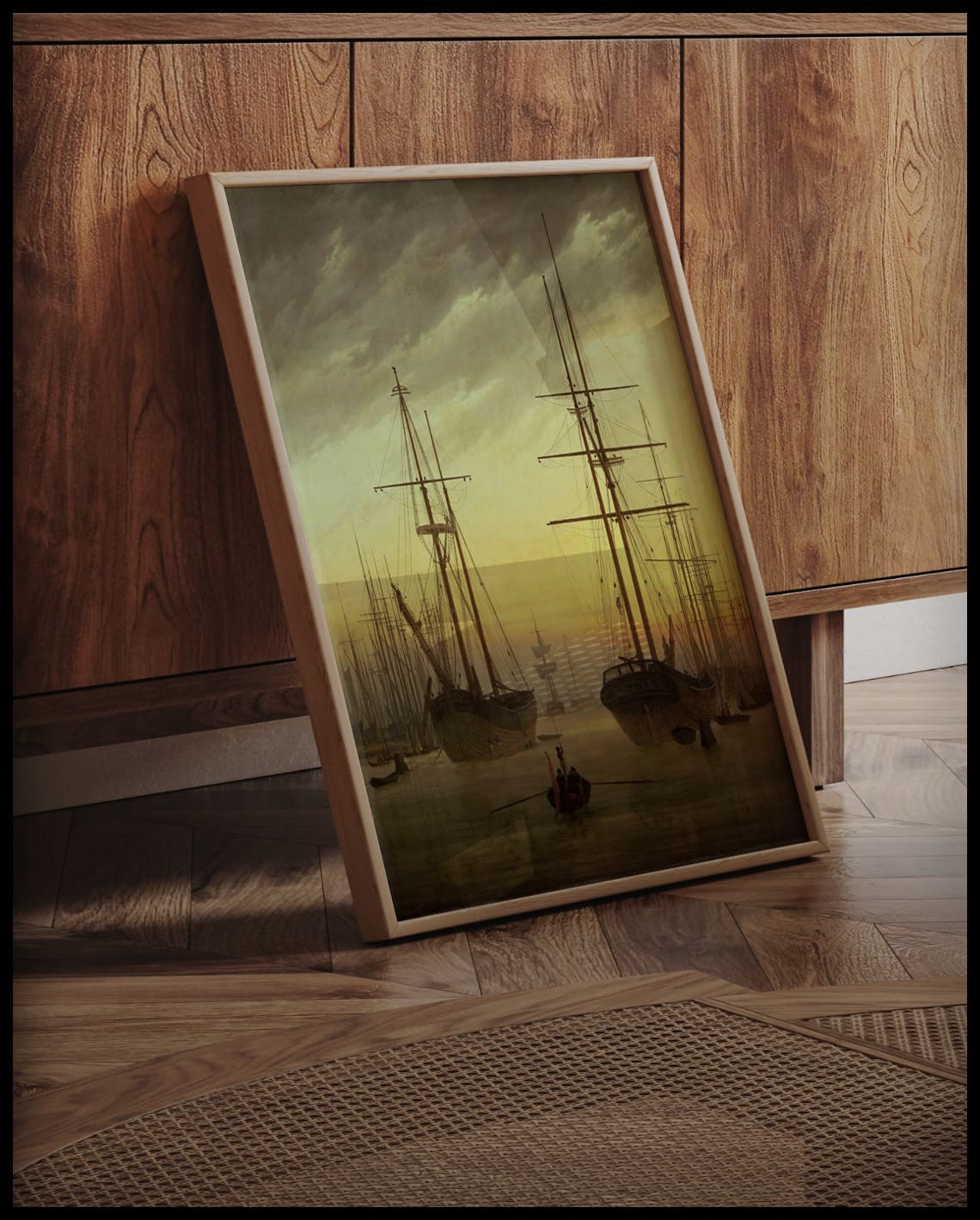 Ein gerahmter Kunstdruck von Schiffen in einem Hafen bei Sonnenuntergang, an einer Holzkommode angelehnt und stehend auf dem Holzboden