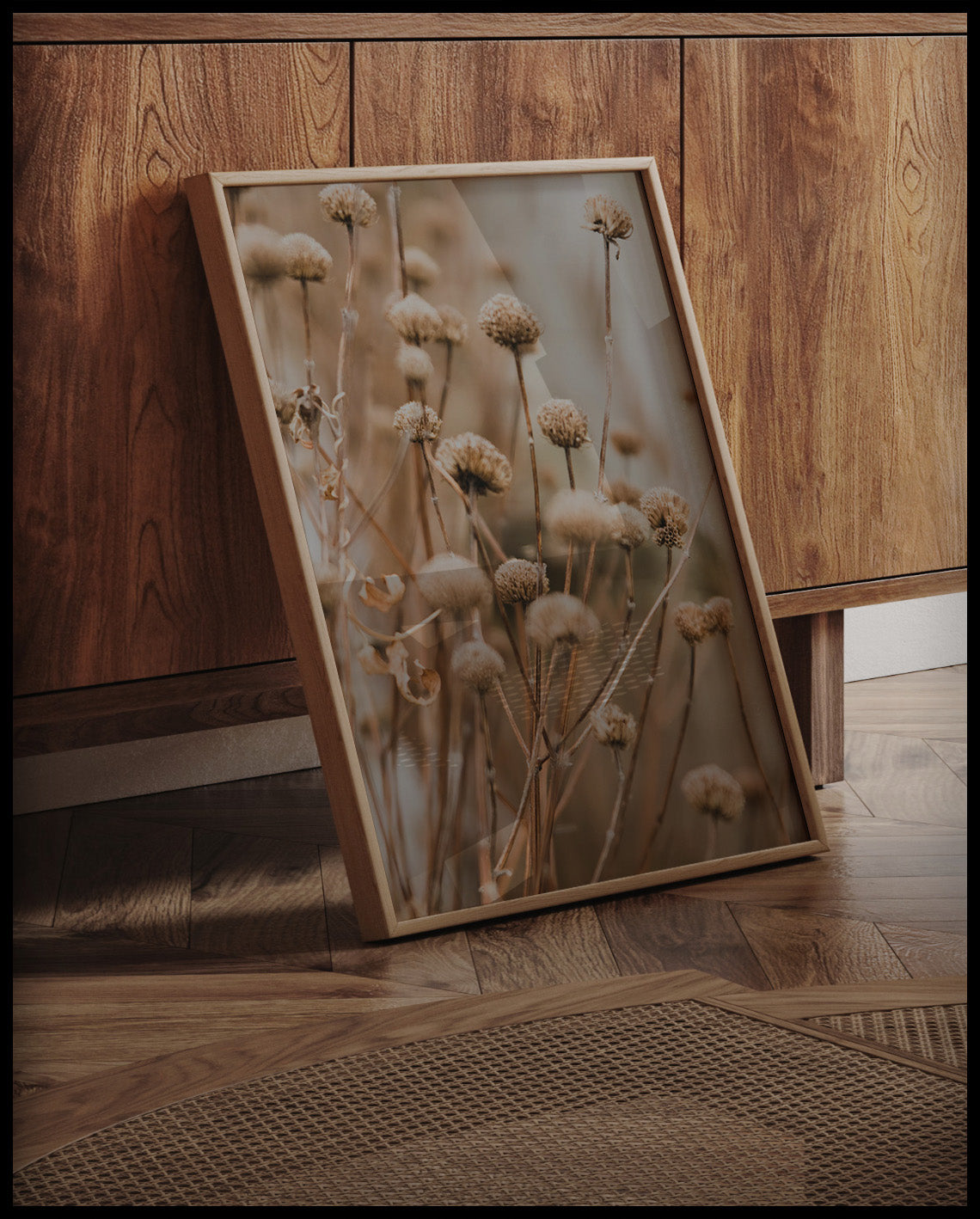 Ein gerahmtes Poster von vertrockneten Blumen in weichen Braun- und Beigetönen, an einer Holzkommode angelehnt und stehend auf dem Holzboden
