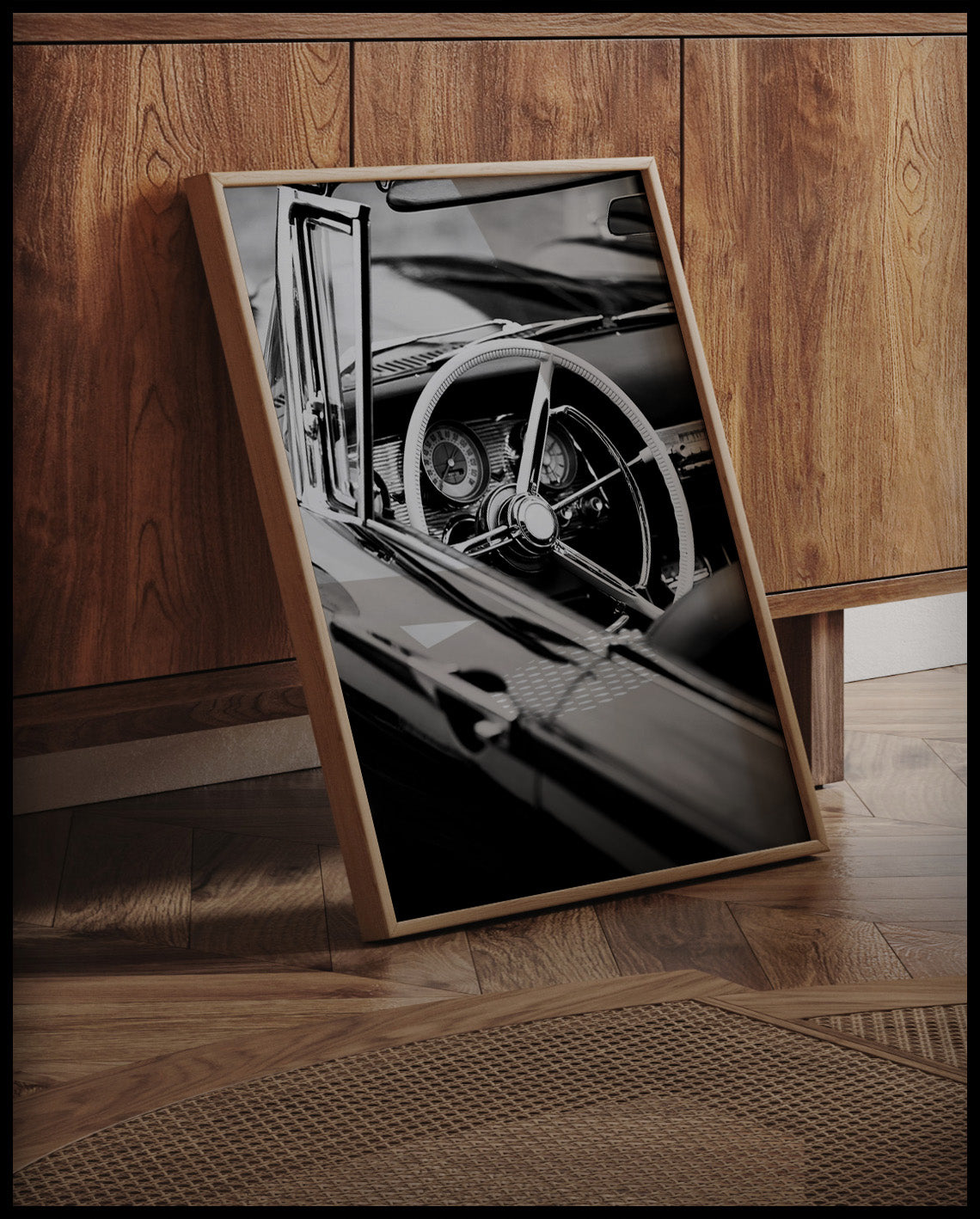 Ein gerahmtes Poster von dem Lenkrad und Armaturenbrett eines klassischen Cabriolets in Schwarz-Weiß, an einer Holzkommode angelehnt und stehend auf dem Holzboden