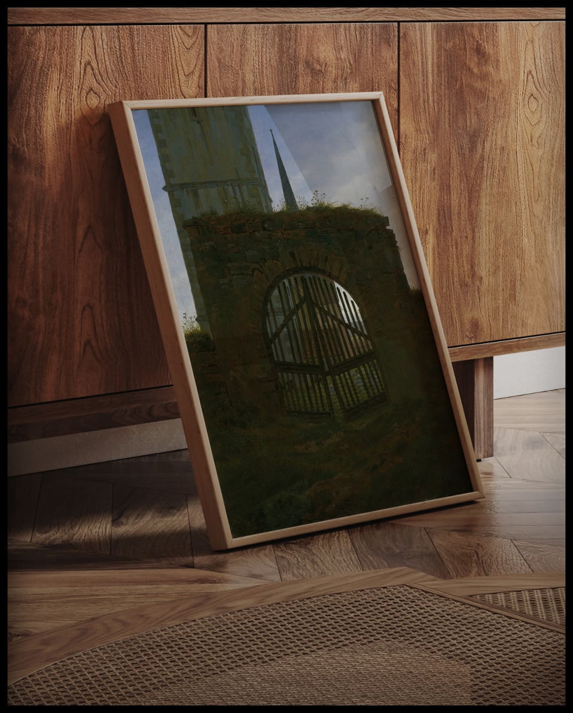 Ein gerahmter Kunstdruck eines Friedhofstors an einer Holzkommode angelehnt und stehend auf dem Holzboden