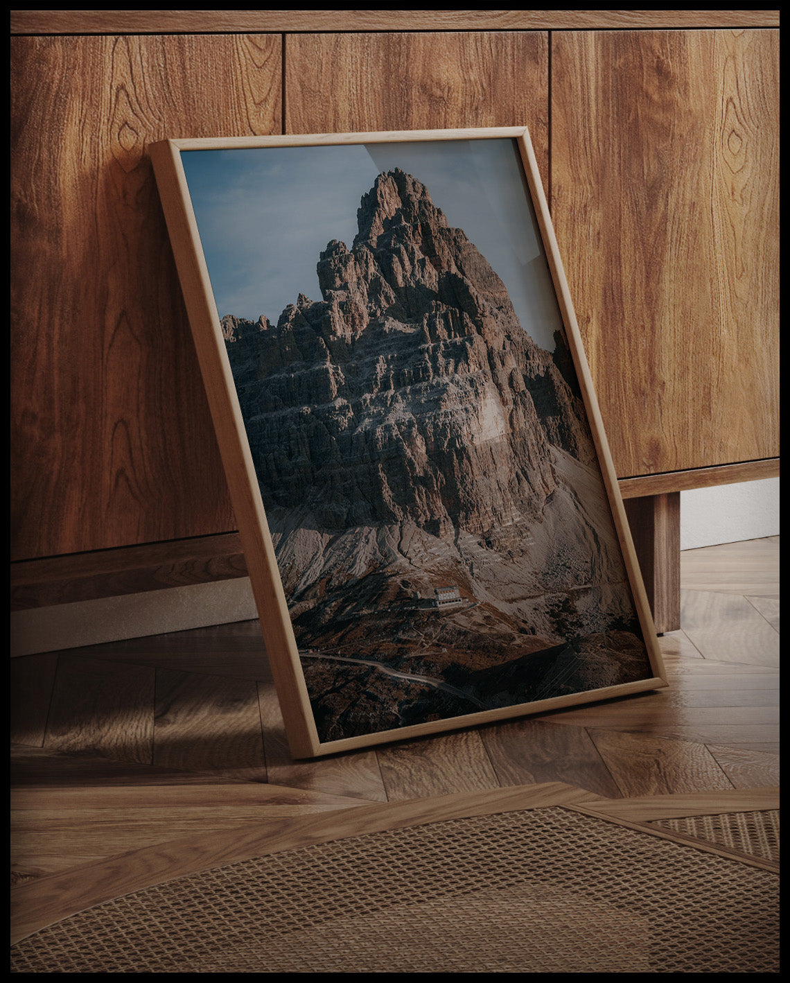 Ein gerahmtes Poster von einem massiven Berg in den Dolomiten, an einer Holzkommode angelehnt und stehend auf dem Holzboden