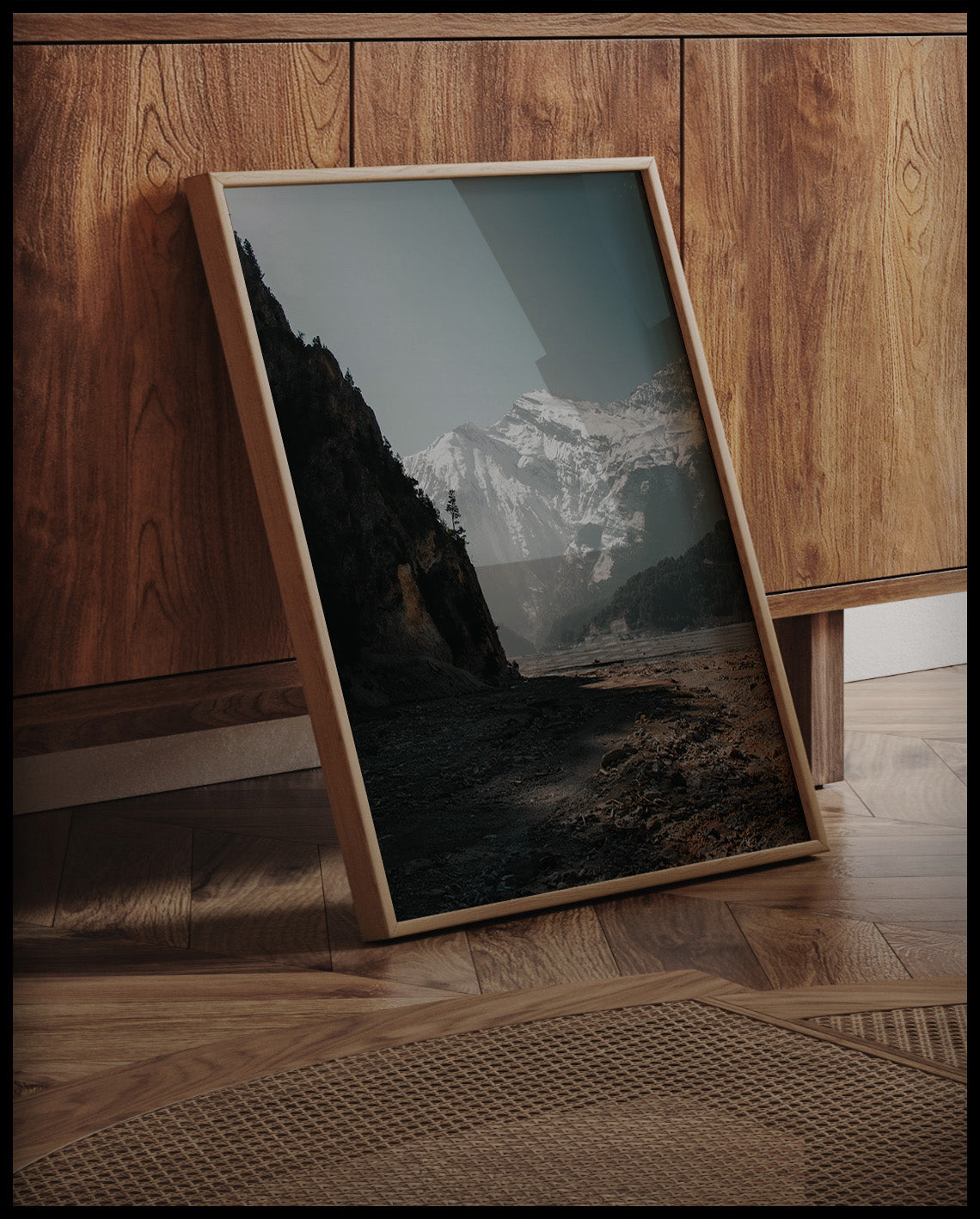 Ein gerahmtes Poster von einem breiten Flussbett in den Dolomiten, umgeben von schneebedeckten Bergen, an einer Holzkommode angelehnt und stehend auf dem Holzboden