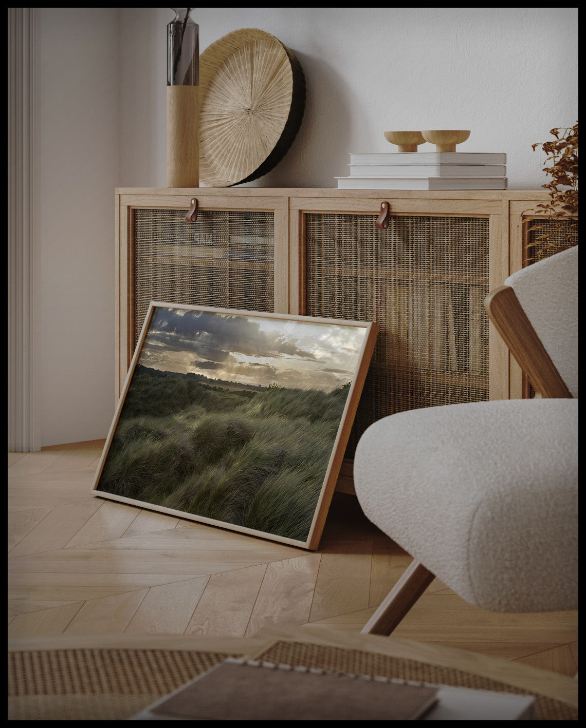 Ein gerahmtes Poster von Gräsern auf einer Düne bei Sonnenuntergang, an einer Holzkommode angelehnt und stehend auf dem Holzboden