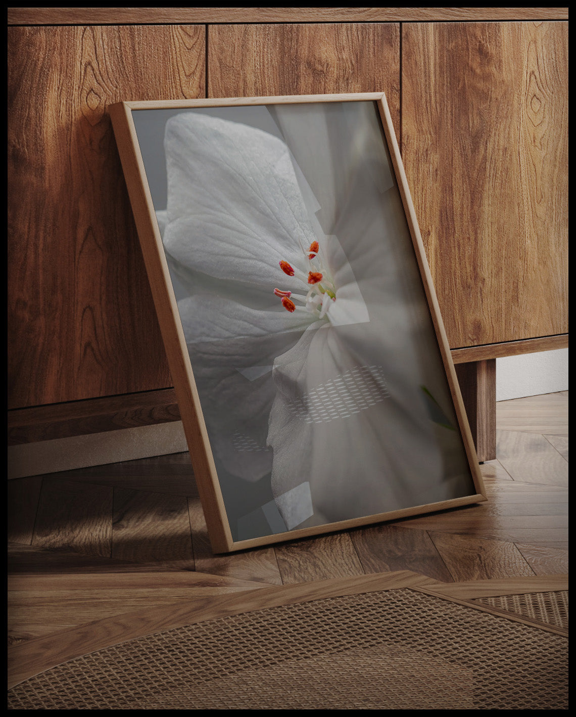 Ein gerahmtes Poster von einer weißen Geranienblüte mit orangen Staubgefäßen in Nahaufnahme, an einer Holzkommode angelehnt und stehend auf dem Holzboden