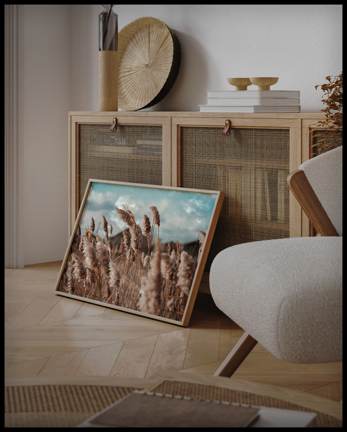 Ein gerahmtes Poster von schilfartigen Pflanzen, die im Wind wehen, an einer Holzkommode angelehnt und stehend auf dem Holzboden