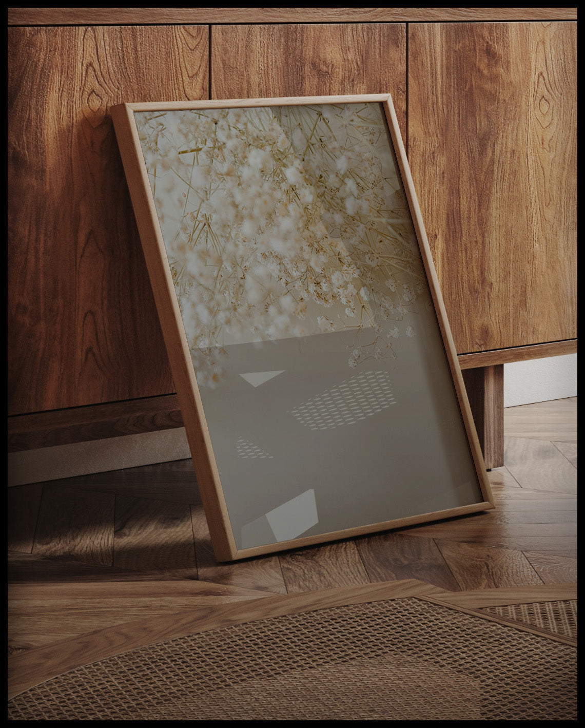 Ein gerahmter Poster von zarten, weißen Gipskrautblüten in einer minimalistischen Anordnung, an einer Holzkommode angelehnt und stehend auf dem Holzboden