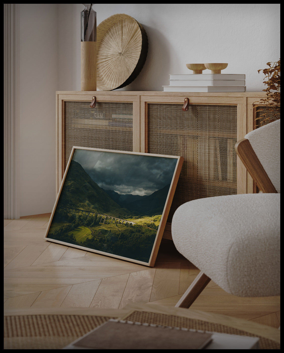 Ein gerahmtes Poster von dem Glenfinnan-Viadukt bei bewölktem Himmel, an einer Holzkommode angelehnt und stehend auf dem Holzboden