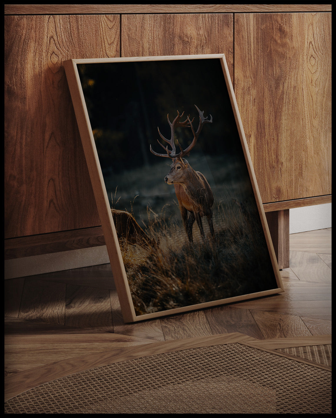 Ein gerahmtes Poster von einem majestätischen Hirsch mit großem Geweih in einer herbstlichen Landschaft, an einer Holzkommode angelehnt und stehend auf dem Holzboden