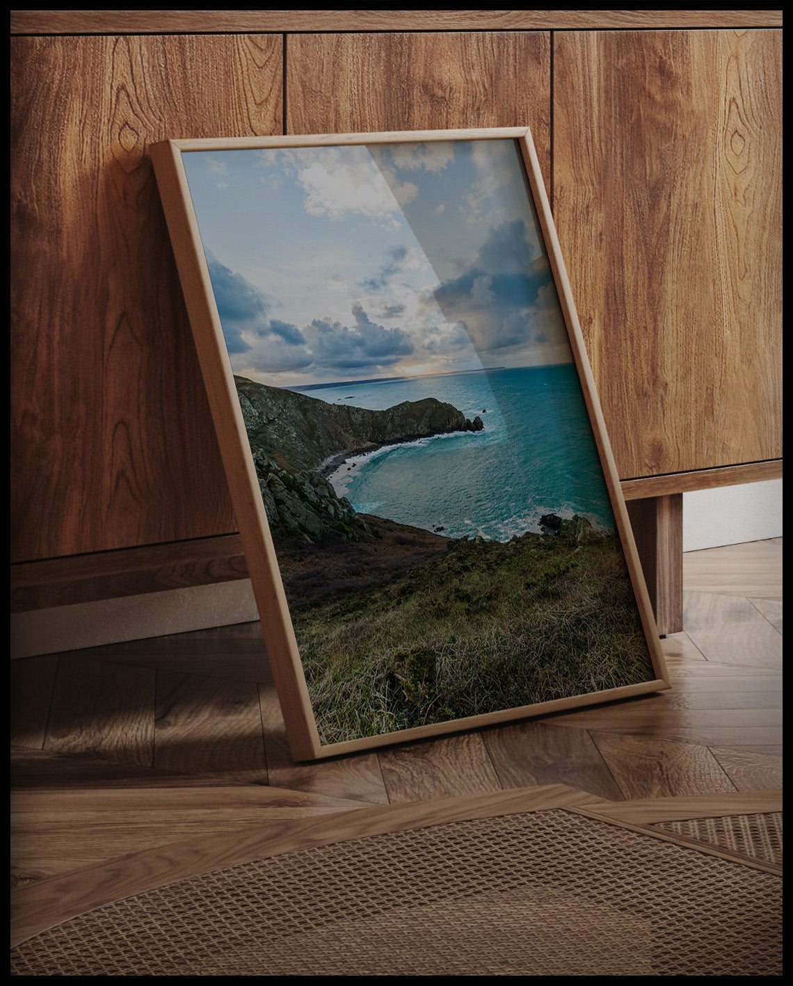 Ein gerahmtes Poster vom Blick einer Bucht über das blaue Meer, an einer Holzkommode angelehnt und stehend auf dem Holzboden