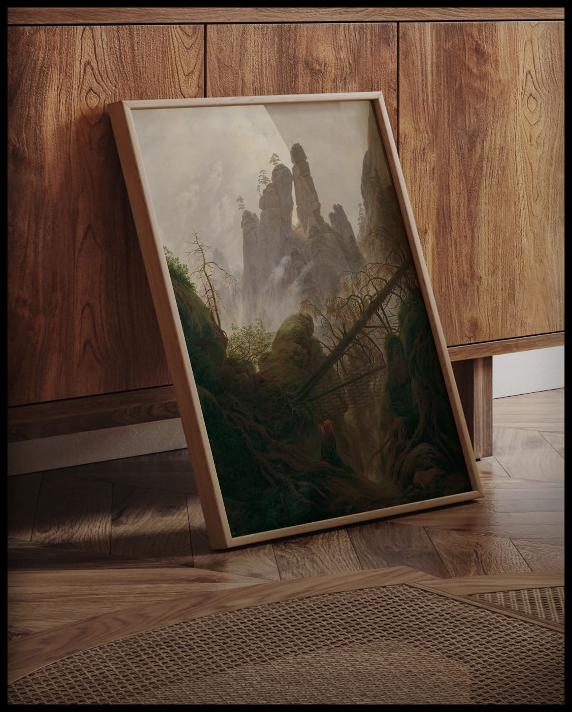 Ein gerahmter Kunstdruck einer felsigen Landschaft mit Bergen und Bäumen, an einer Holzkommode angelehnt und stehend auf dem Holzboden
