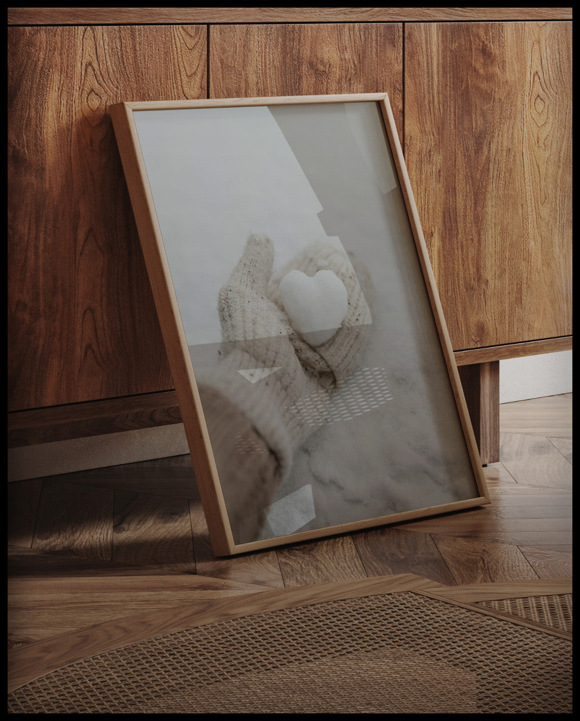 Ein gerahmtes Poster von einer behandschuhten Hand, die ein kleines Herz aus Schnee hält, an einer Holzkommode angelehnt und stehend auf dem Holzboden