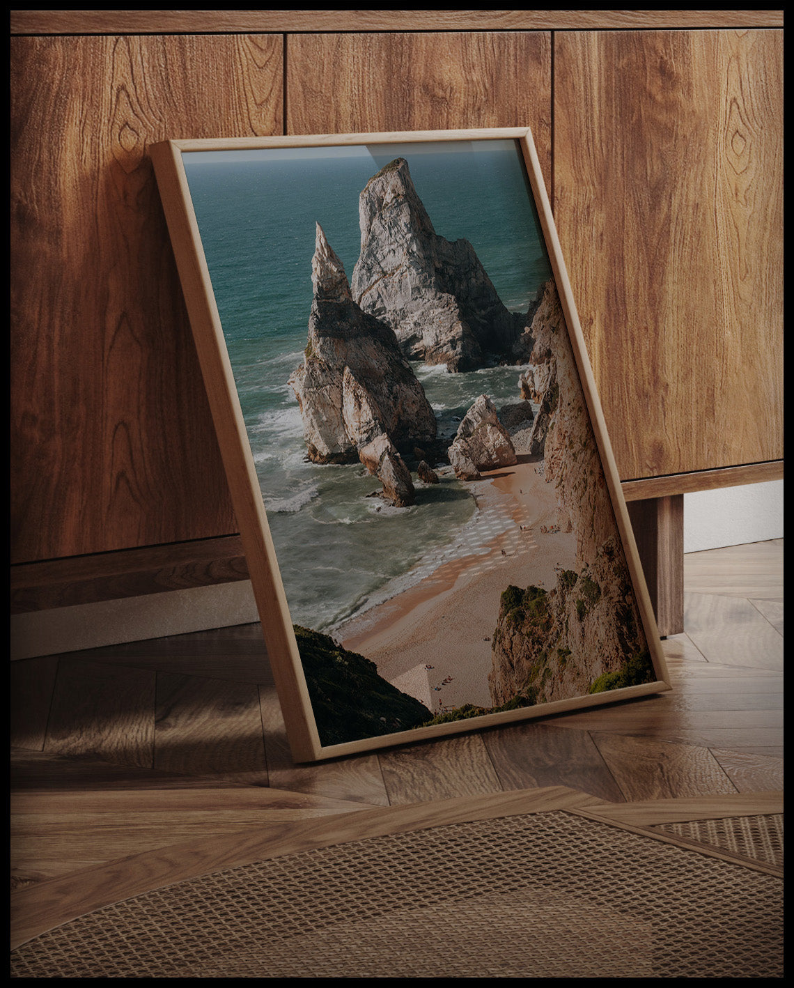 Ein gerahmtes Poster von hohen Felsformationen im Meer an einem Strand, an einer Holzkommode angelehnt und stehend auf dem Holzboden