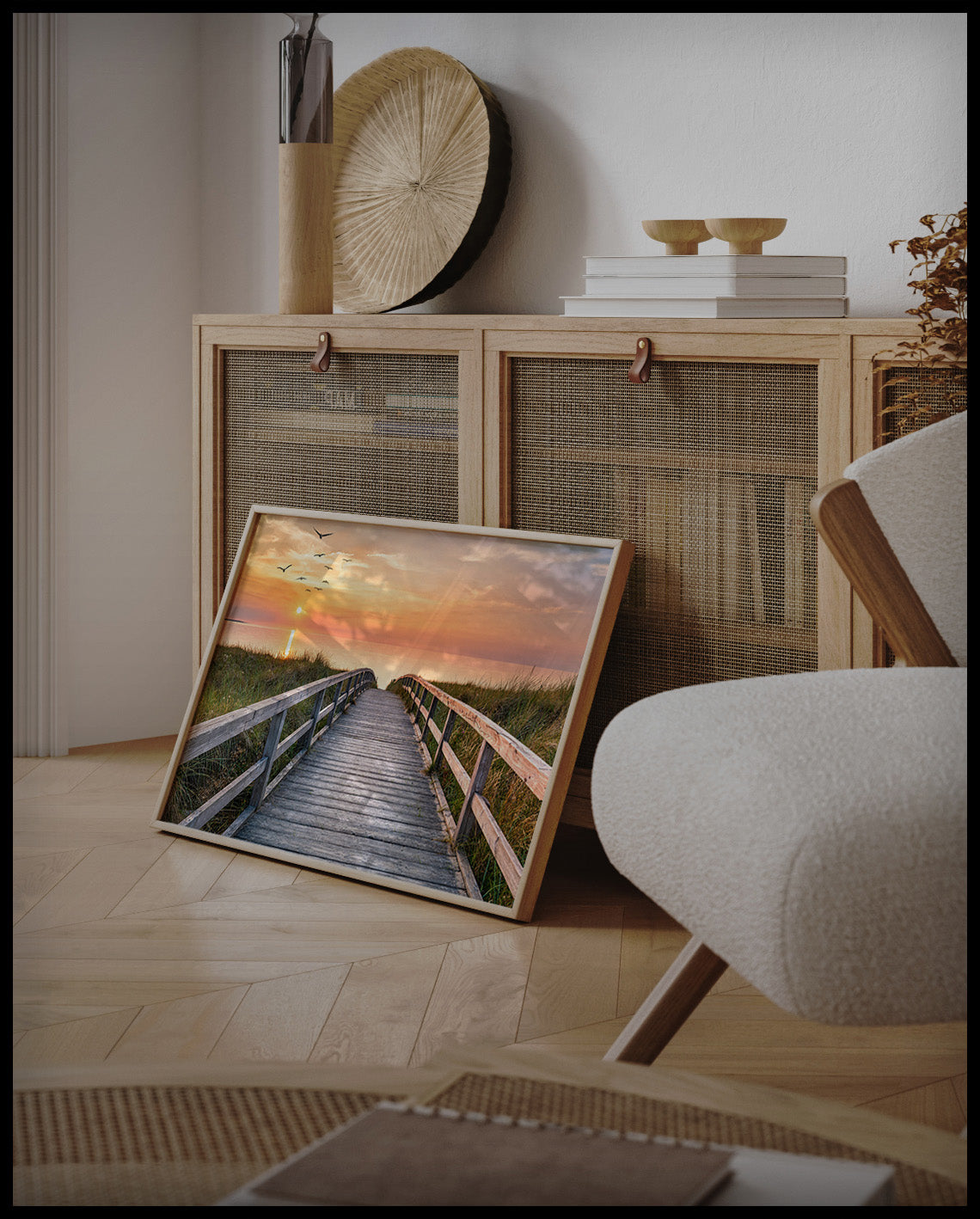 Ein gerahmtes Poster von einem Holzsteg im Sonnenuntergang, der über Dünen zum Strand führt, an einer Holzkommode angelehnt und stehend auf dem Holzboden