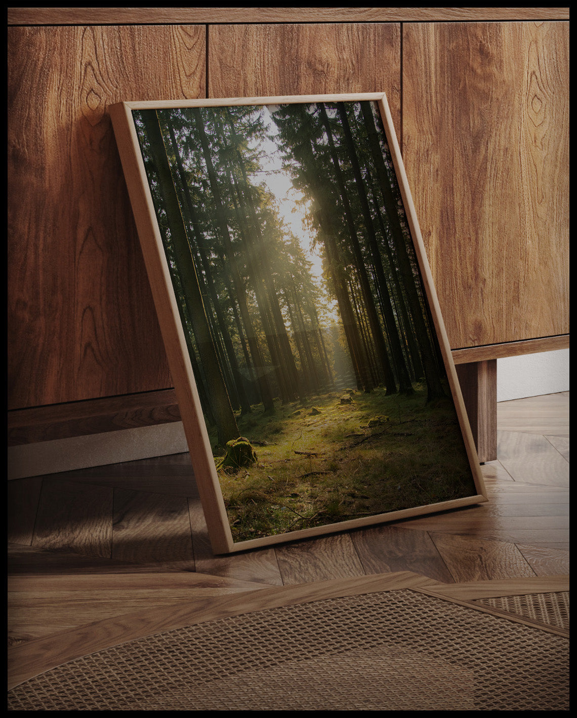 Ein gerahmtes Poster von einer Lichtung im Wald mit hohen Nadelbäumen, an einer Holzkommode angelehnt und stehend auf dem Holzboden