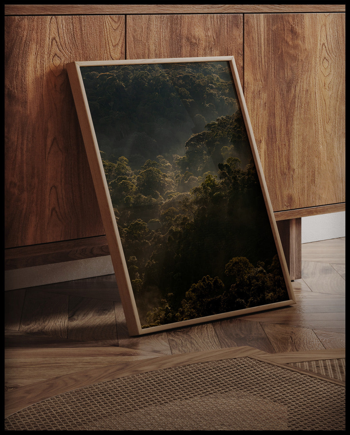 Ein gerahmtes Poster vom Sonnenaufgang über einem dichten Wald, an einer Holzkommode angelehnt und stehend auf dem Holzboden