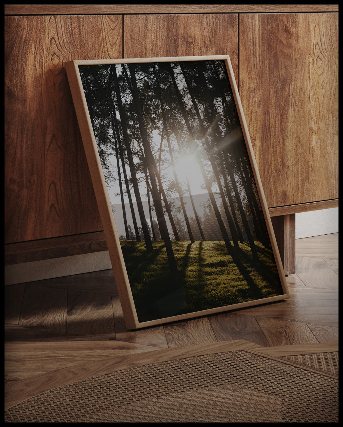Ein gerahmtes Poster von Sonnenstrahlen die durch einige schmale Bäume hindurch scheinen, an einer Holzkommode angelehnt und stehend auf dem Holzboden