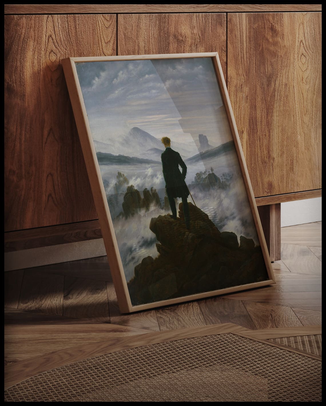 Ein gerahmter Kunstdruck des Wanderers über dem Nebelmeer, an einer Holzkommode angelehnt und stehend auf dem Boden