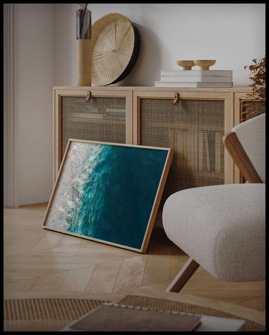 Ein gerahmtes Poster aus der Vogelperspektive vom blauen Meer und schaumigen Wellen, an einer Holzkommode angelehnt und stehend auf dem Holzboden