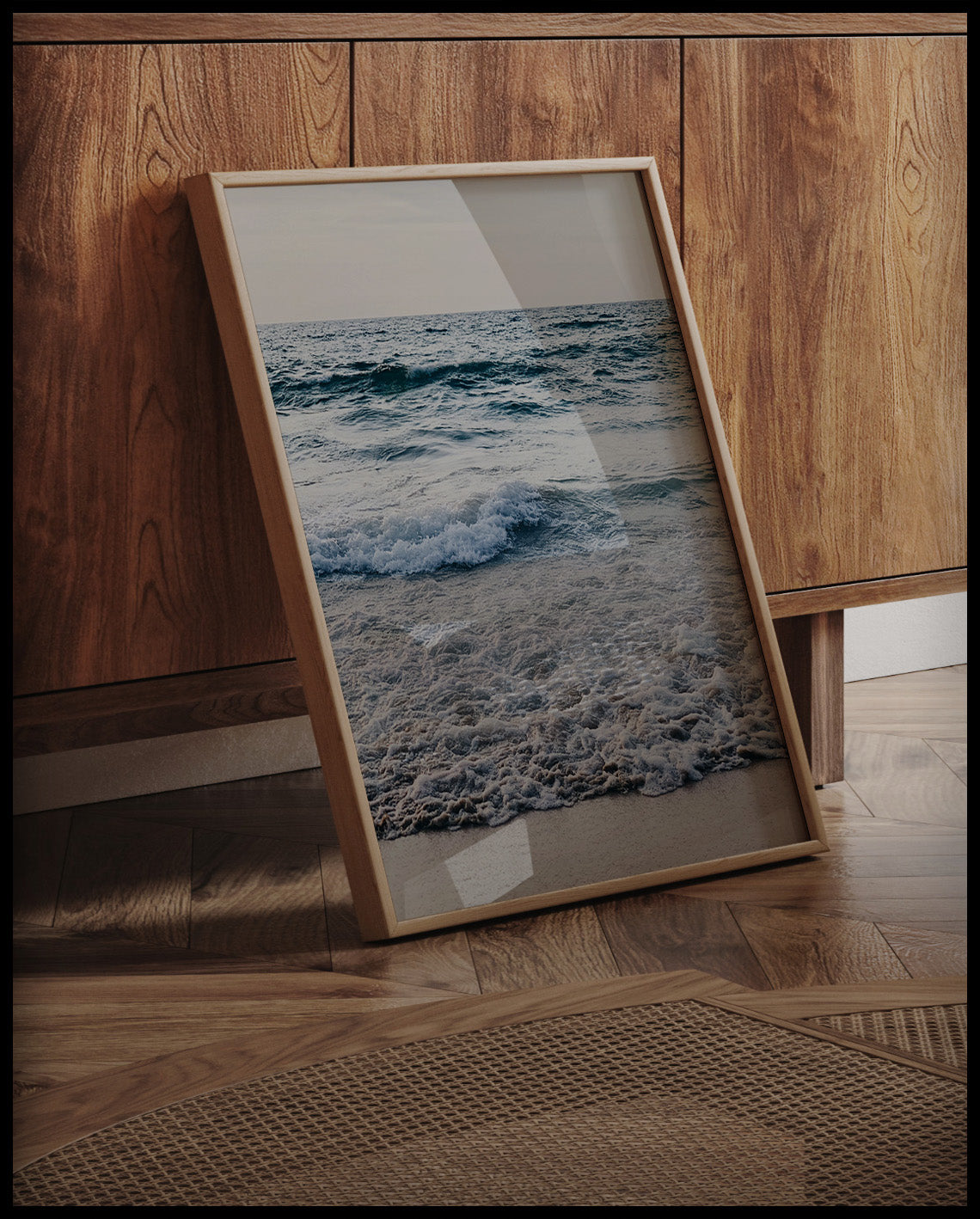 Ein gerahmtes Poster von schaumigen Wellen am Strand, an einer Holzkommode angelehnt und stehend auf dem Holzboden