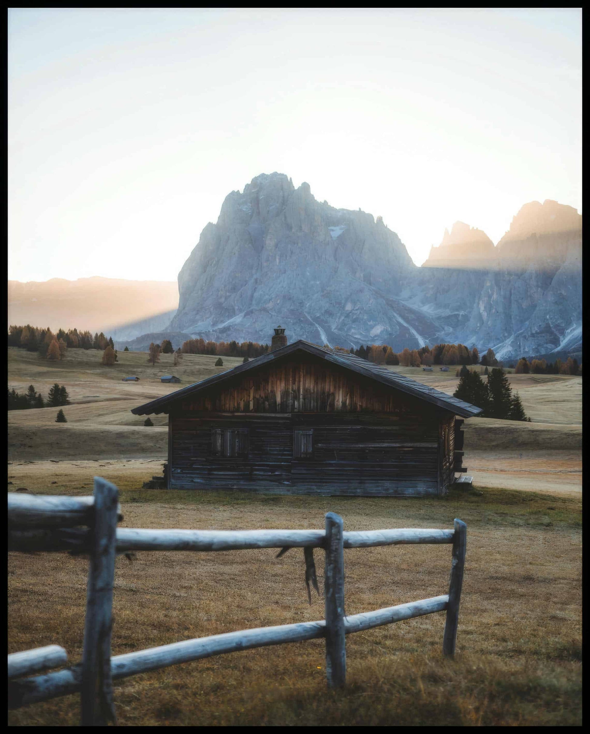 Ein Poster von einer rustikalen Hütte in einer herbstlichen Berglandschaft.