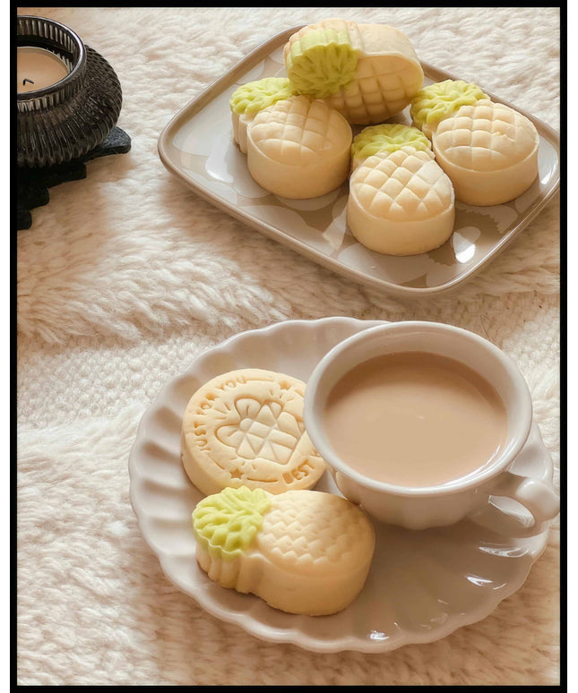 Ein Poster von einer Tasse Kaffee und Ananas-geformten Keksen auf einem Teller, arrangiert auf einem weichen, flauschigen Untergrund.