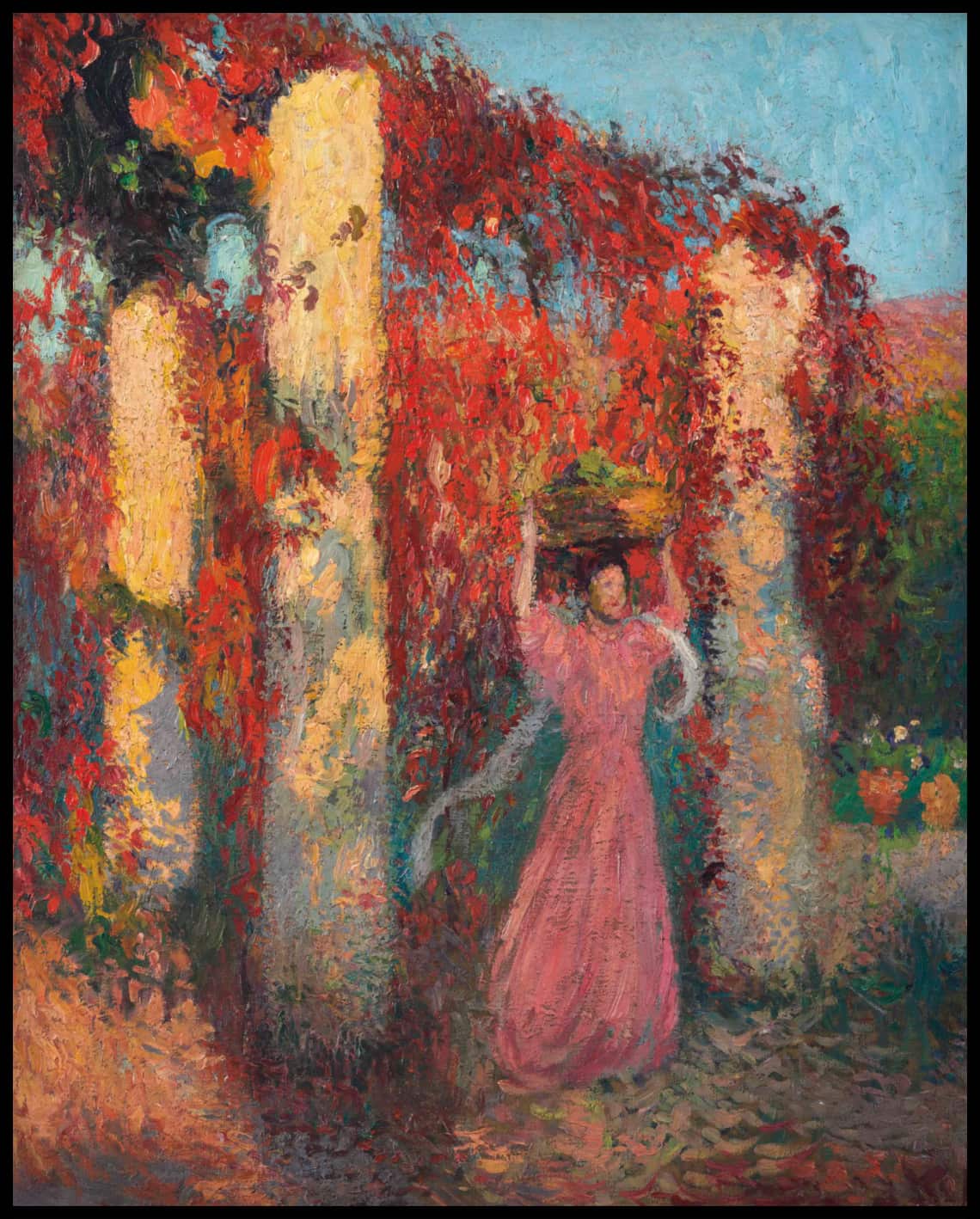 Jeune femme portant une corbeille sur la tête devant une pergola de vigne-vierge rouge