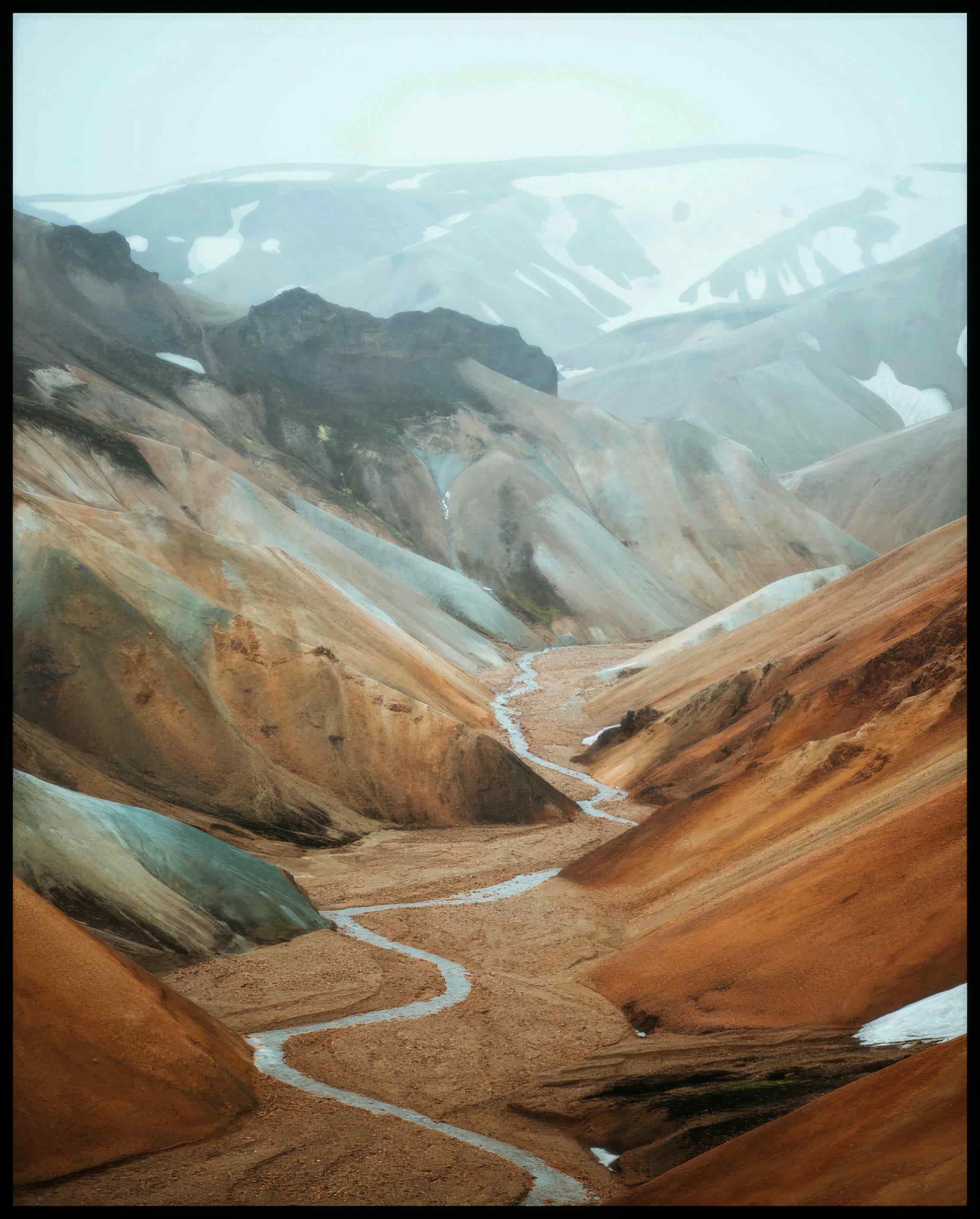 Ein Poster von einem Tal mit einem Fluss und orangenen Bergen.