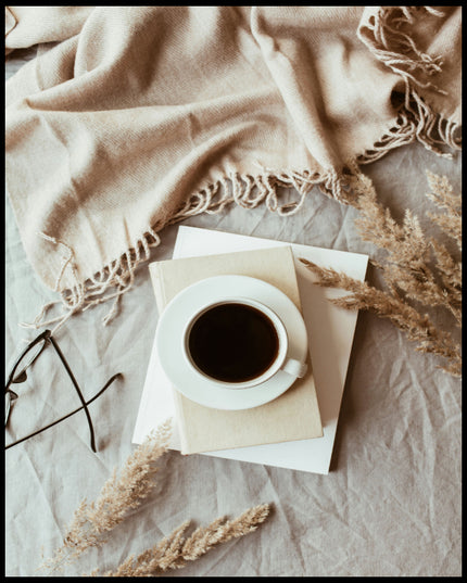 Ein Poster von einer Tasse Kaffee auf einem Stapel Bücher, umgeben von einem beigen Tuch und getrockneten Pflanzen.