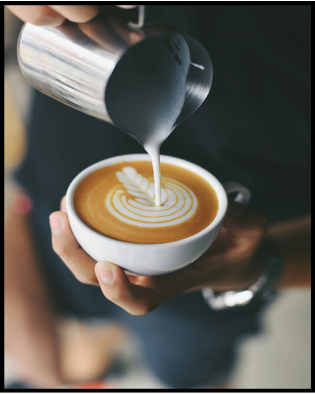 Ein Poster von einem Barista, der kunstvoll Milch in eine Tasse Kaffee gießt und ein Muster kreiert.