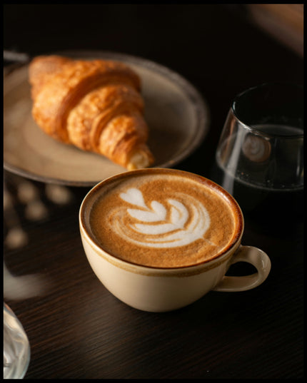 Ein Poster von einer Tasse Kaffee Latte neben einem Croissant und einem Glas Wasser.