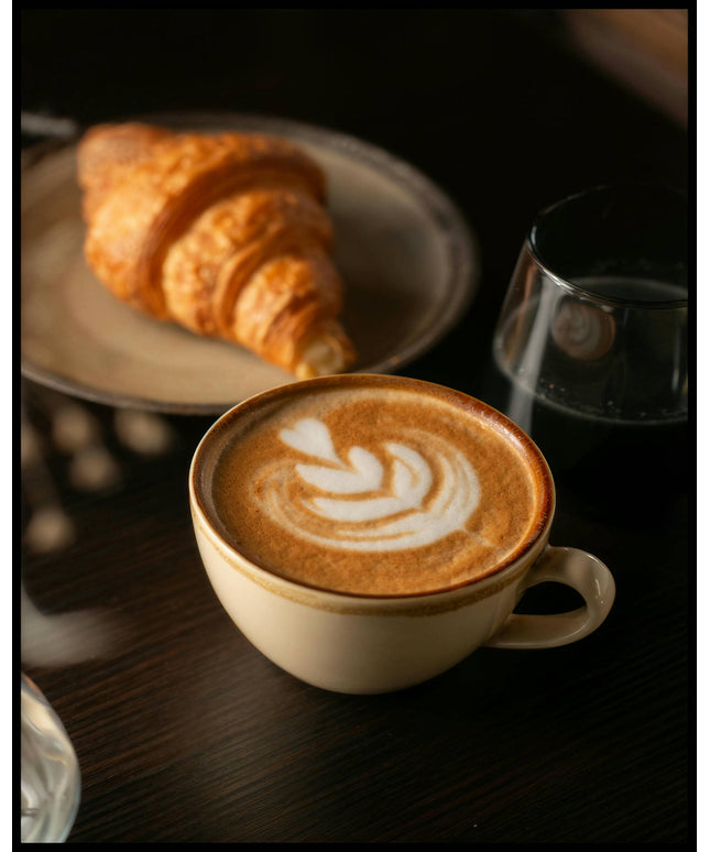 Ein Poster von einer Tasse Kaffee Latte neben einem Croissant und einem Glas Wasser.