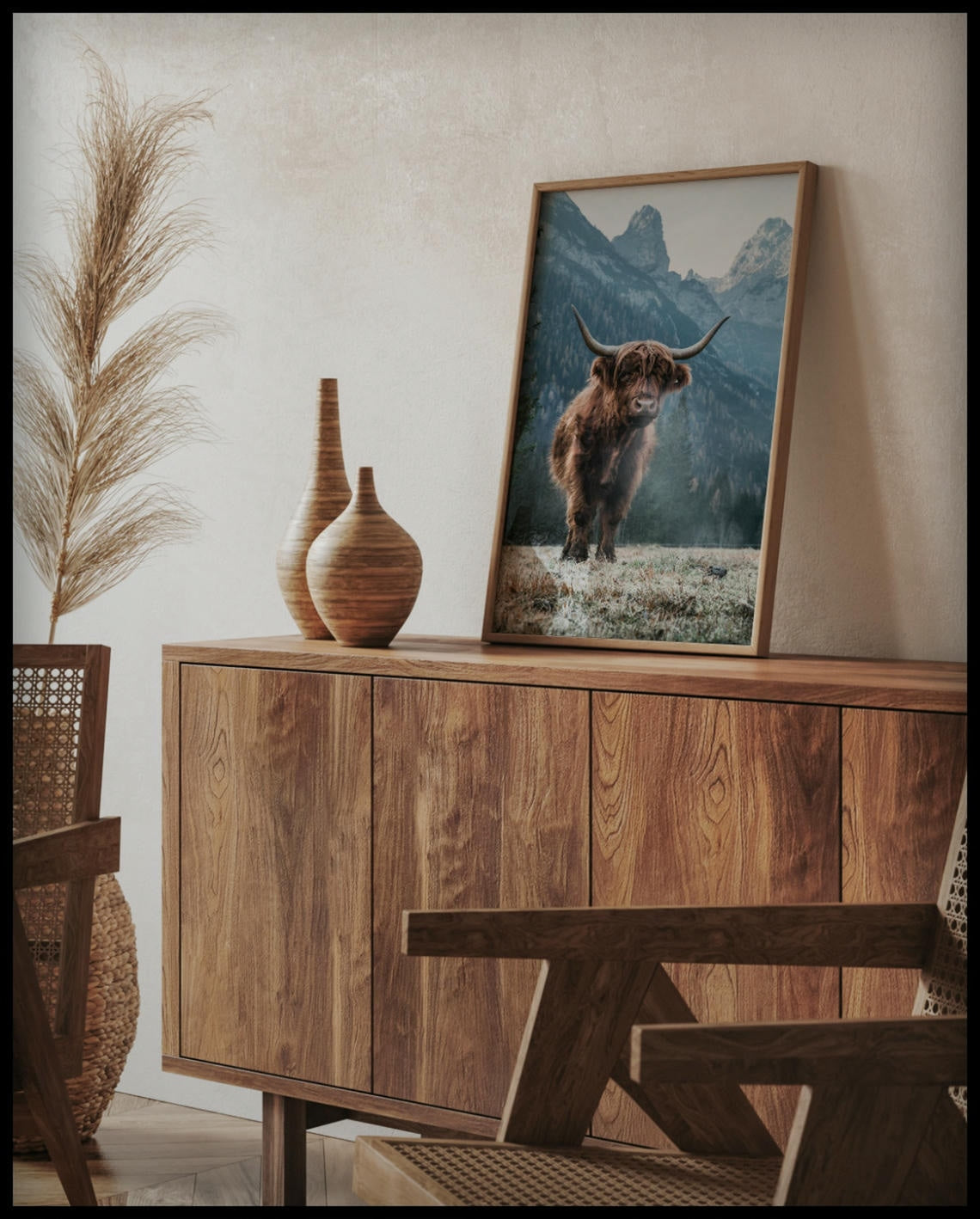 Ein gerahmtes Poster von einem Highland-Rind, das vor einer Berglandschaft steht, auf einer Holzkommode an die Wand angelehnt