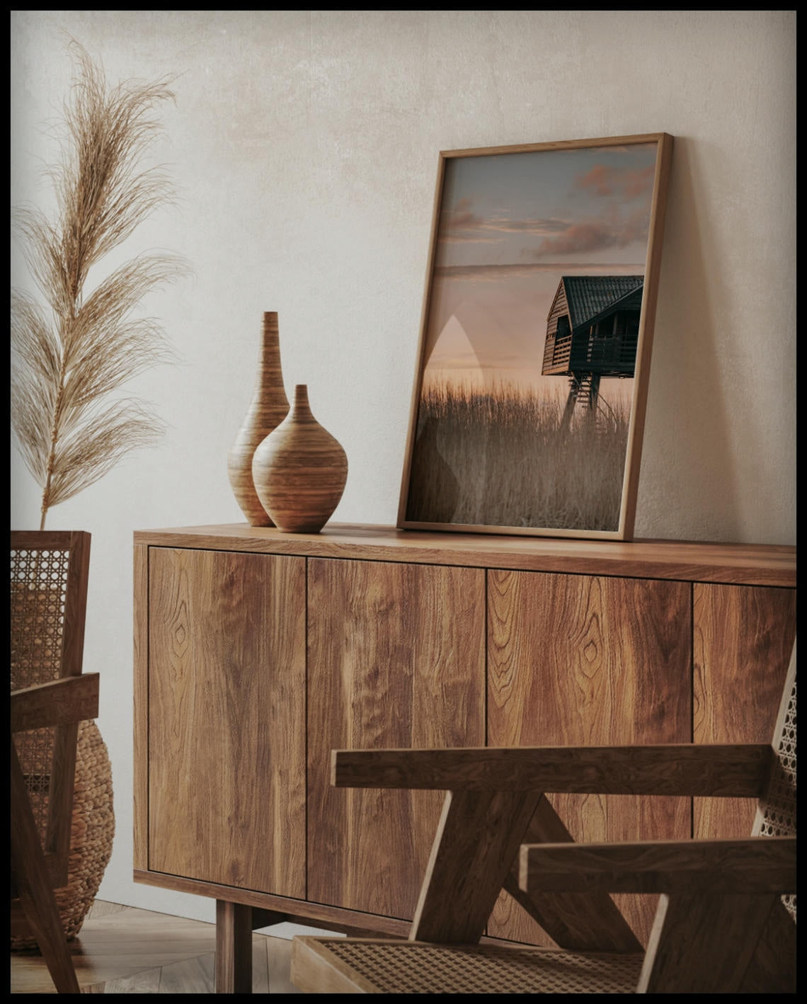 Ein gerahmtes Poster von einer Hütte am Strand in den Dünen bei Sonnenuntergang, auf einer Holzkommode an die Wand angelehnt