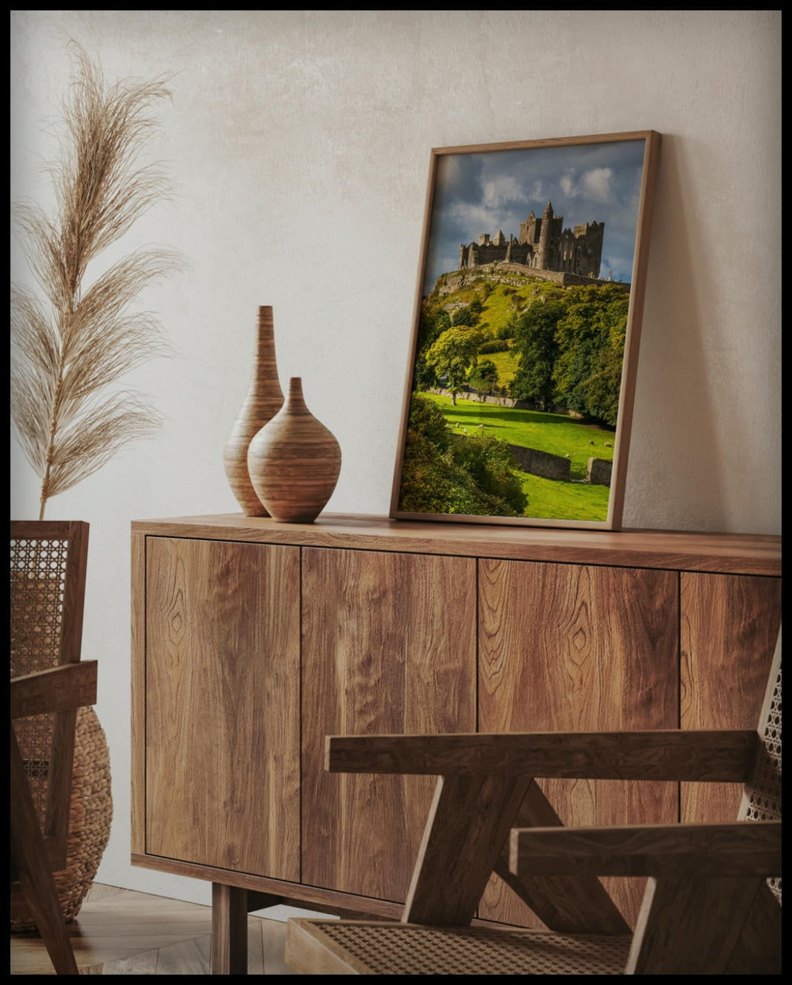 Ein gerahmtes Poster von den Ruinen des Rock of Cashel auf einem Hügel in Irland, umgeben von grünen Wiesen und Bäumen, auf einer Holzkommode an die Wand angelehnt