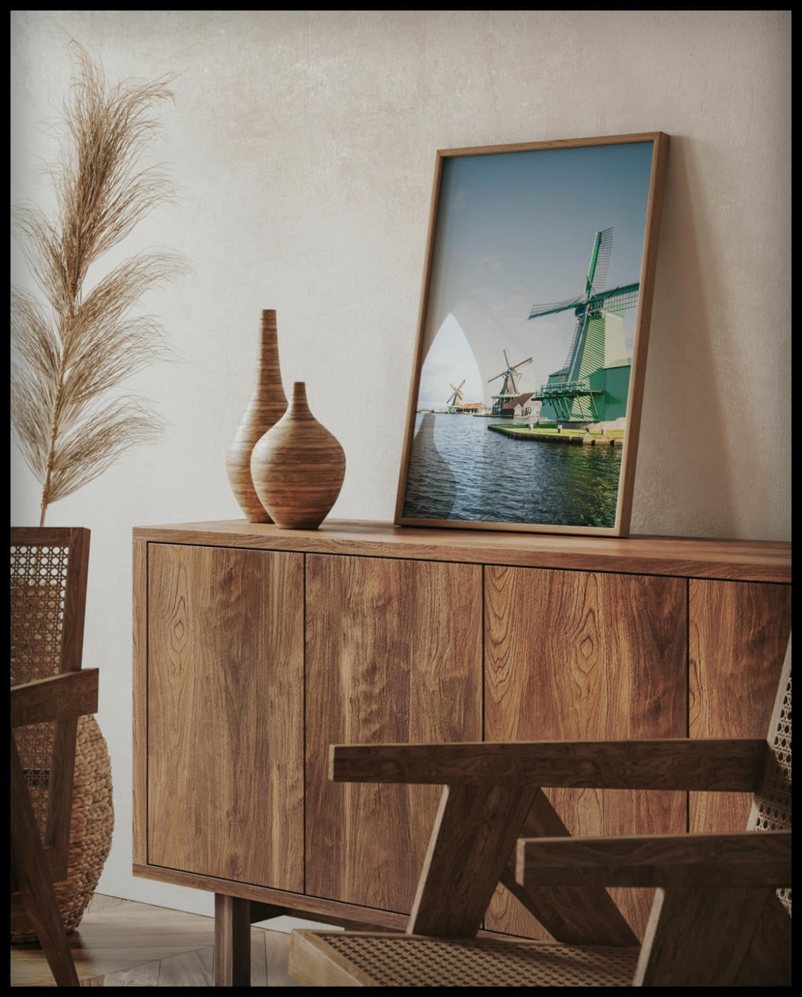 Ein gerahmtes Poster von drei Windmühlen aus Holz die am Wasser stehen, auf einer Holzkommode an die Wand angelehnt
