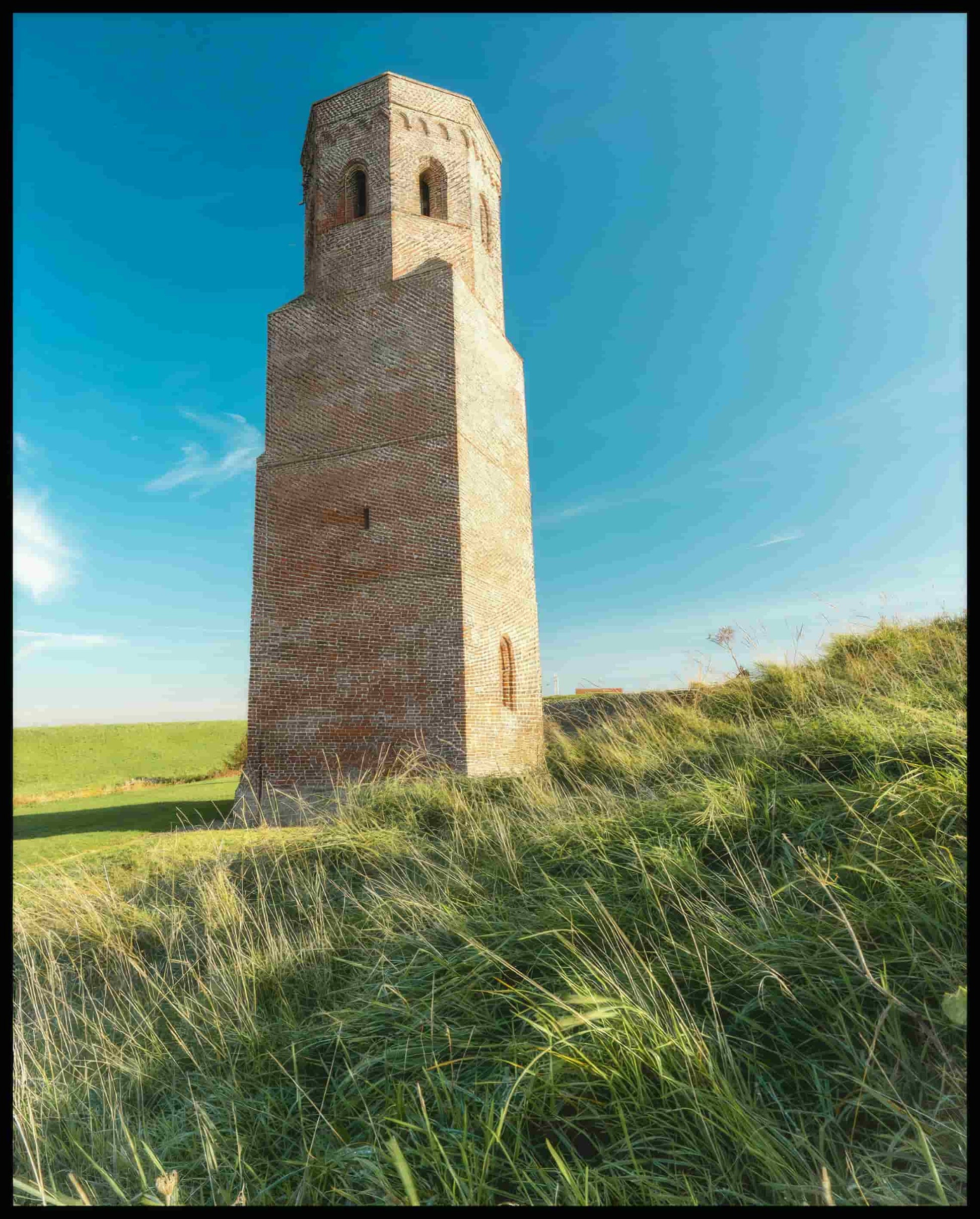 Ein Poster von einem steinernen Turm auf einer grünen, hügeligen Wiese.