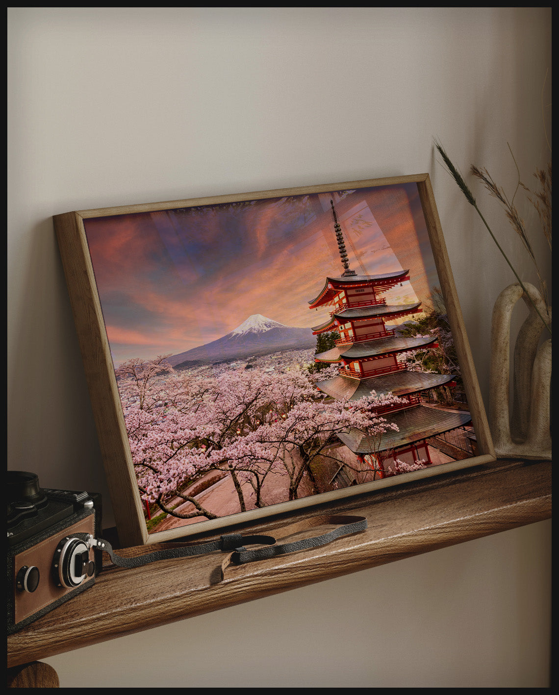 Ein gerahmtes Poster von der Chureito-Pagode vor dem Fuji-Berg bei Sonnenuntergang, umgeben von Kirschblüten, auf einem Holzregal an die Wand angelehnt