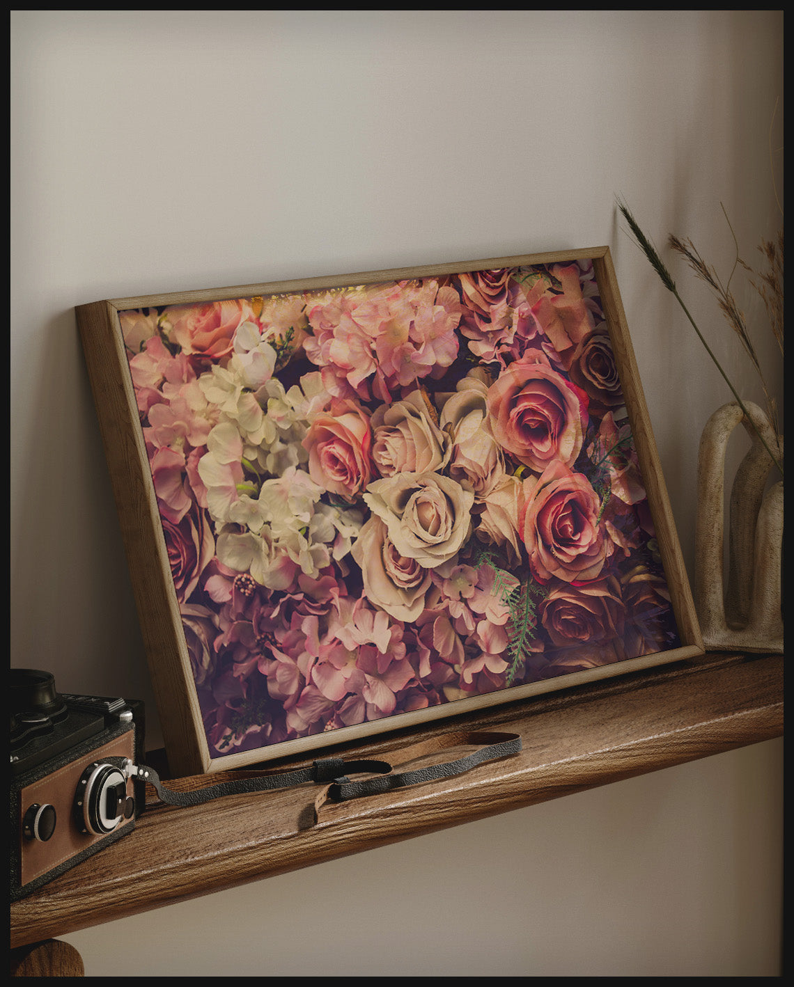 Ein gerahmtes Poster von einer Fülle rosa Blumen in einem üppigen Blumenstrauß, auf einem Holzregal an die Wand angelehnt