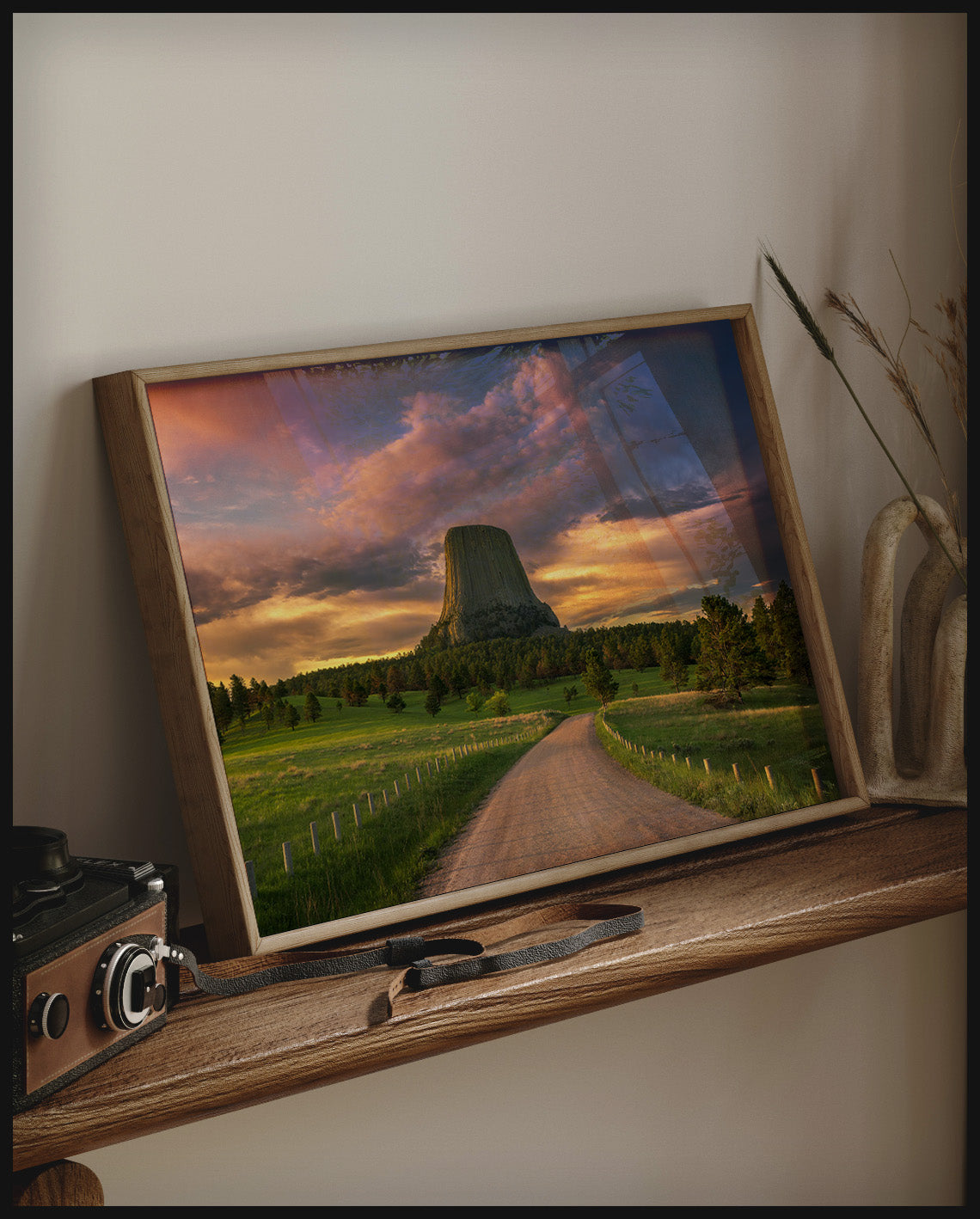 Ein gerahmtes Poster vom Devils Tower bei Sonnenuntergang, auf einem Holzregal an die Wand angelehnt