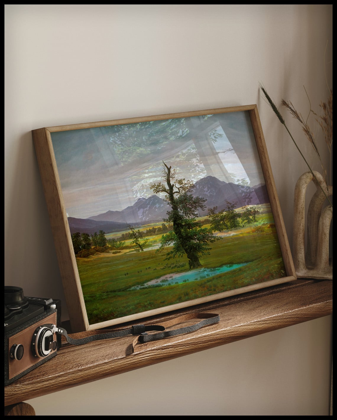 Ein gerahmter Kunstdruck von einem einsamen Baum auf einer Wiese, auf einem Holzregal an die Wand angelehnt