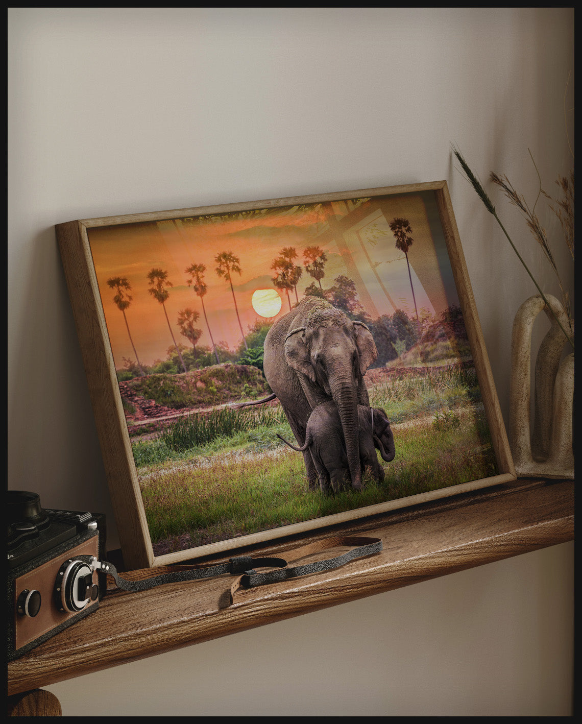 Ein gerahmtes Poster von zwei Elefanten bei Sonnenuntergang in Afrika, auf einem Holzregal an die Wand angelehnt