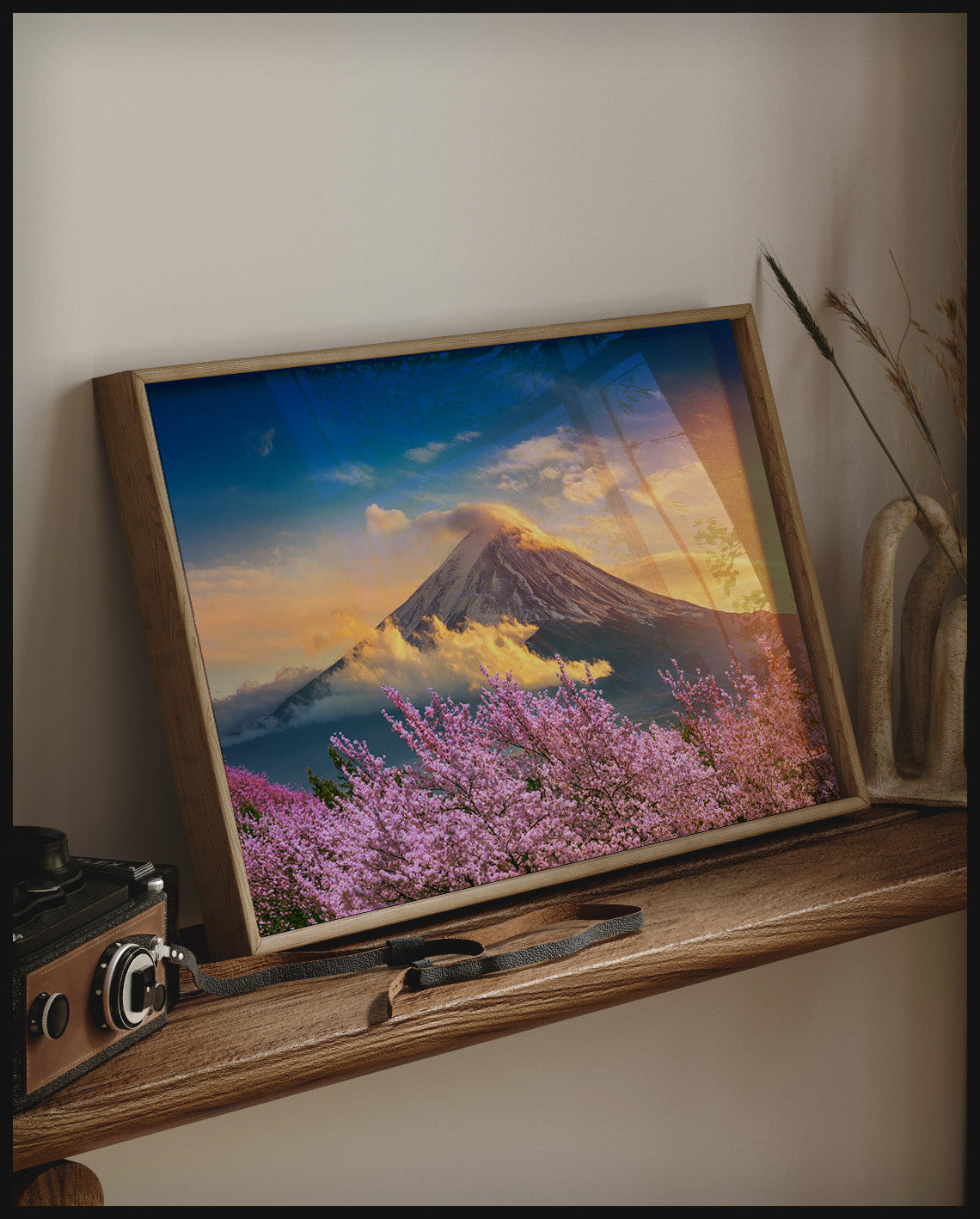 Ein gerahmtes Poster von einem blühenden Kirschbaumfeld vor dem Berg Fuji, auf einem Holzregal an die Wand angelehnt