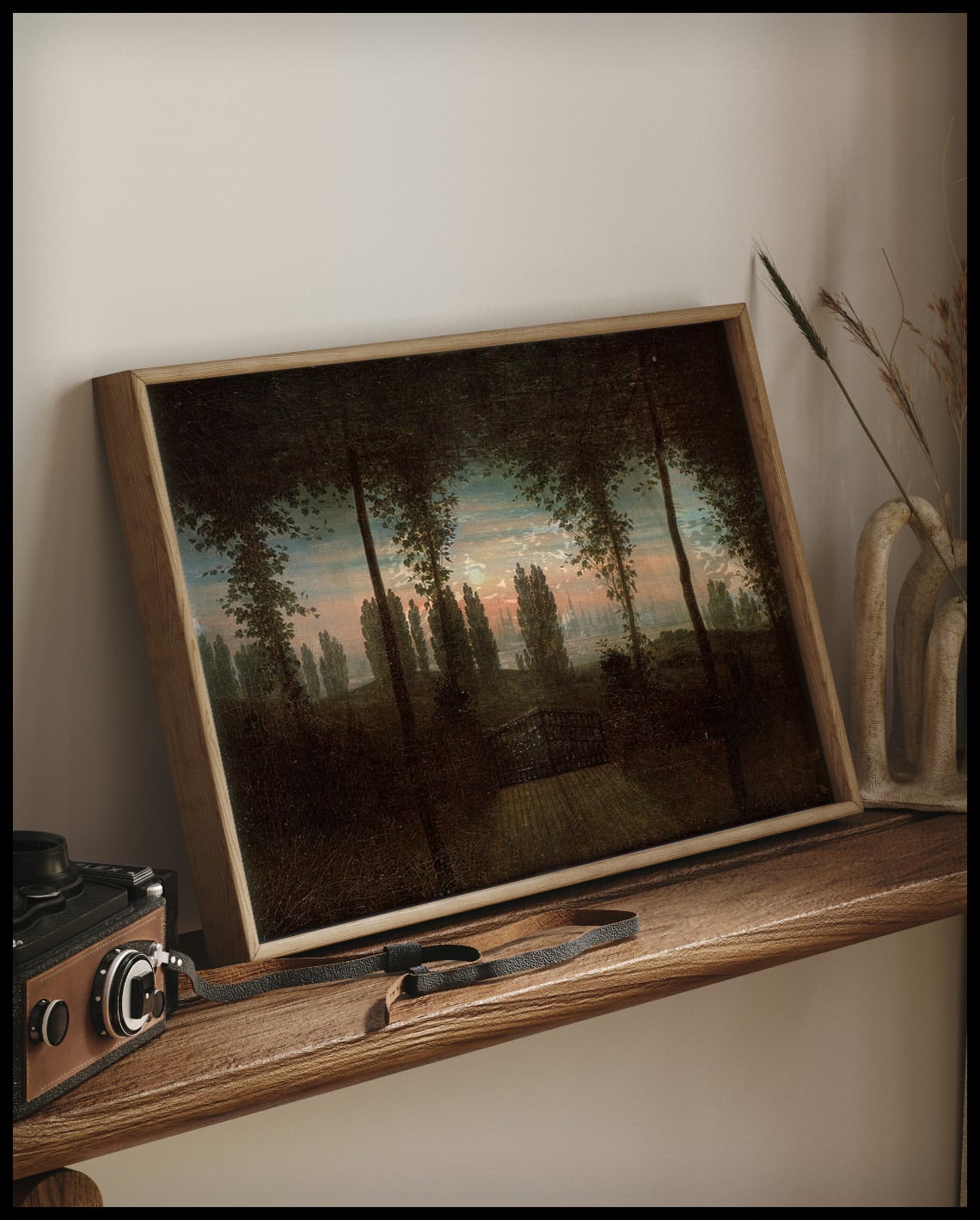 Ein gerahmter Kunstdruck von einer eisernen Zauntür und einer weiten Landschaft, auf einem Holzregal an die Wand angelehnt