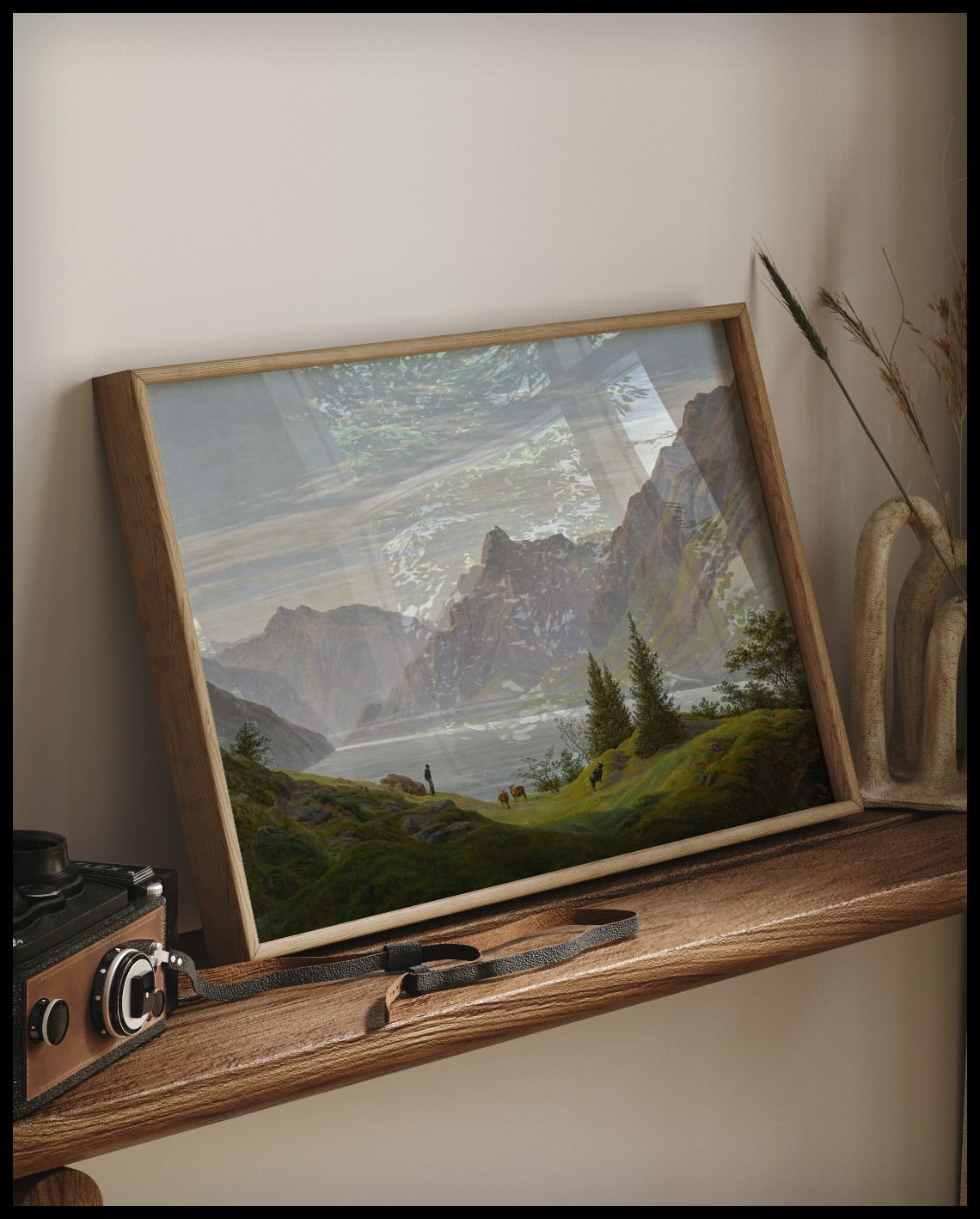 Ein gerahmter Kunstdruck von einer steilen Berglandschaft mit einem Gebirgssee am Morgen, auf einem Holzregal an die Wand angelehnt
