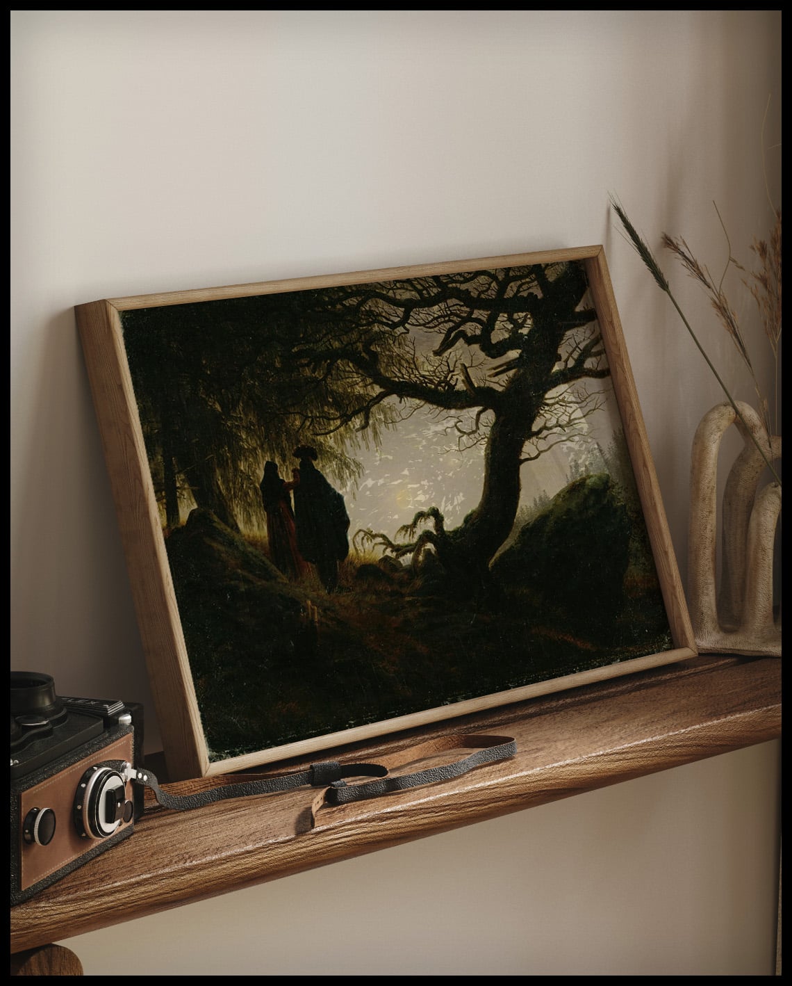 Ein gerahmter Kunstdruck von einem Mann und einer Frau neben einem Baum die den Mond betrachten, auf einem Holzregal an die Wand angelehnt