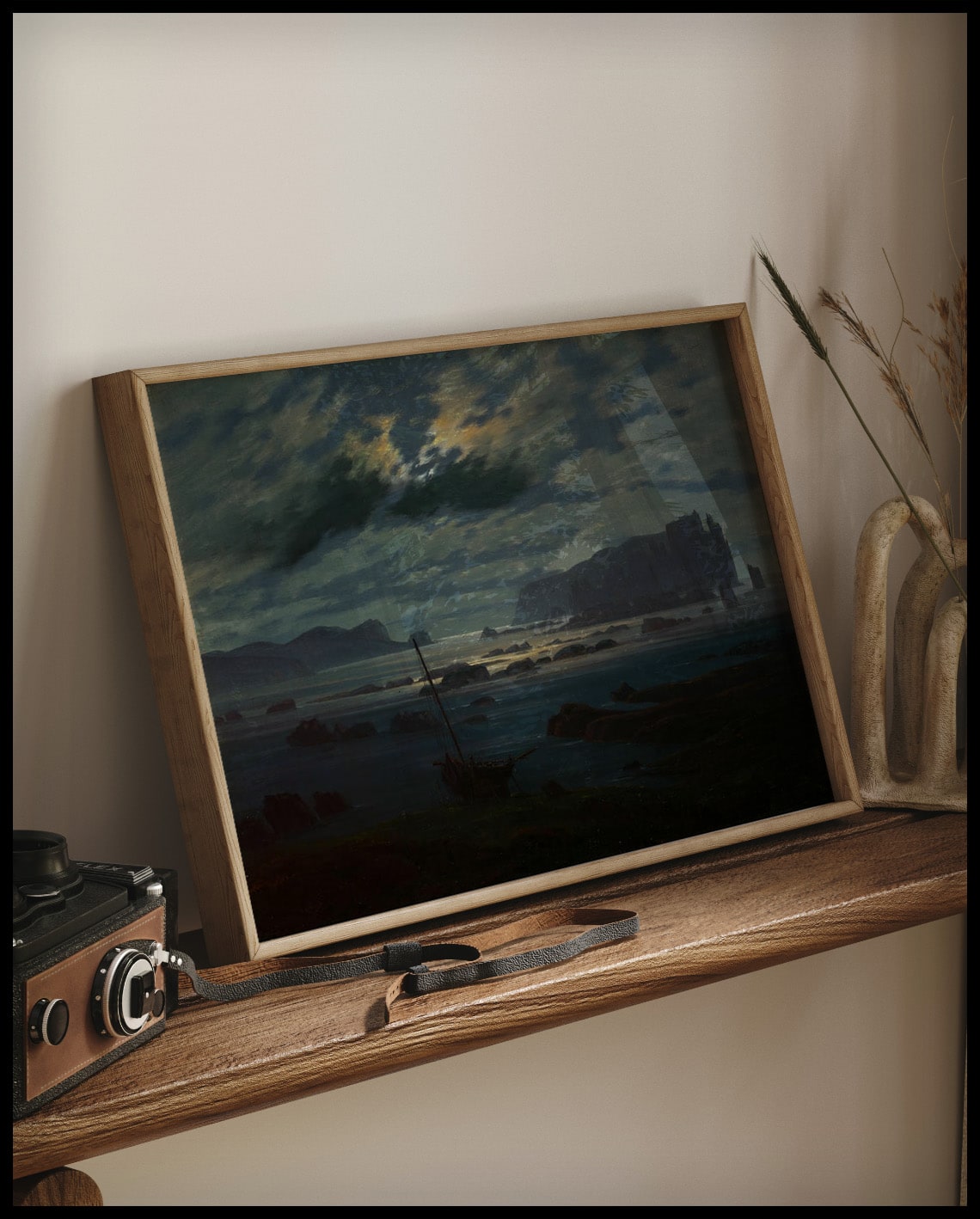 Ein gerahmter Kunstdruck von einer düsteren Küstenlandschaft an der Nordsee im Mondlicht, auf einem Holzregal an die Wand angelehnt